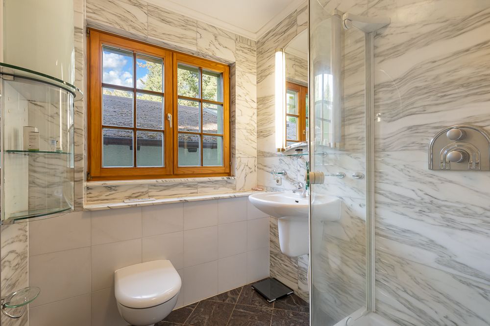 Modernes Badezimmer mit Dusche, WC, Waschbecken und Fenster mit Holzrahmen.