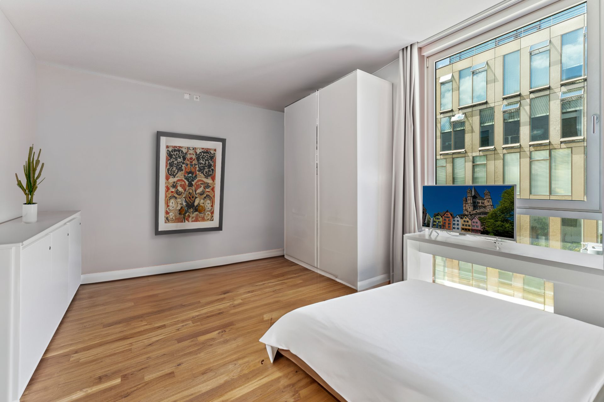Modernes Schlafzimmer mit Holzfußboden, weißem Schrank, Bett und großem Fenster.