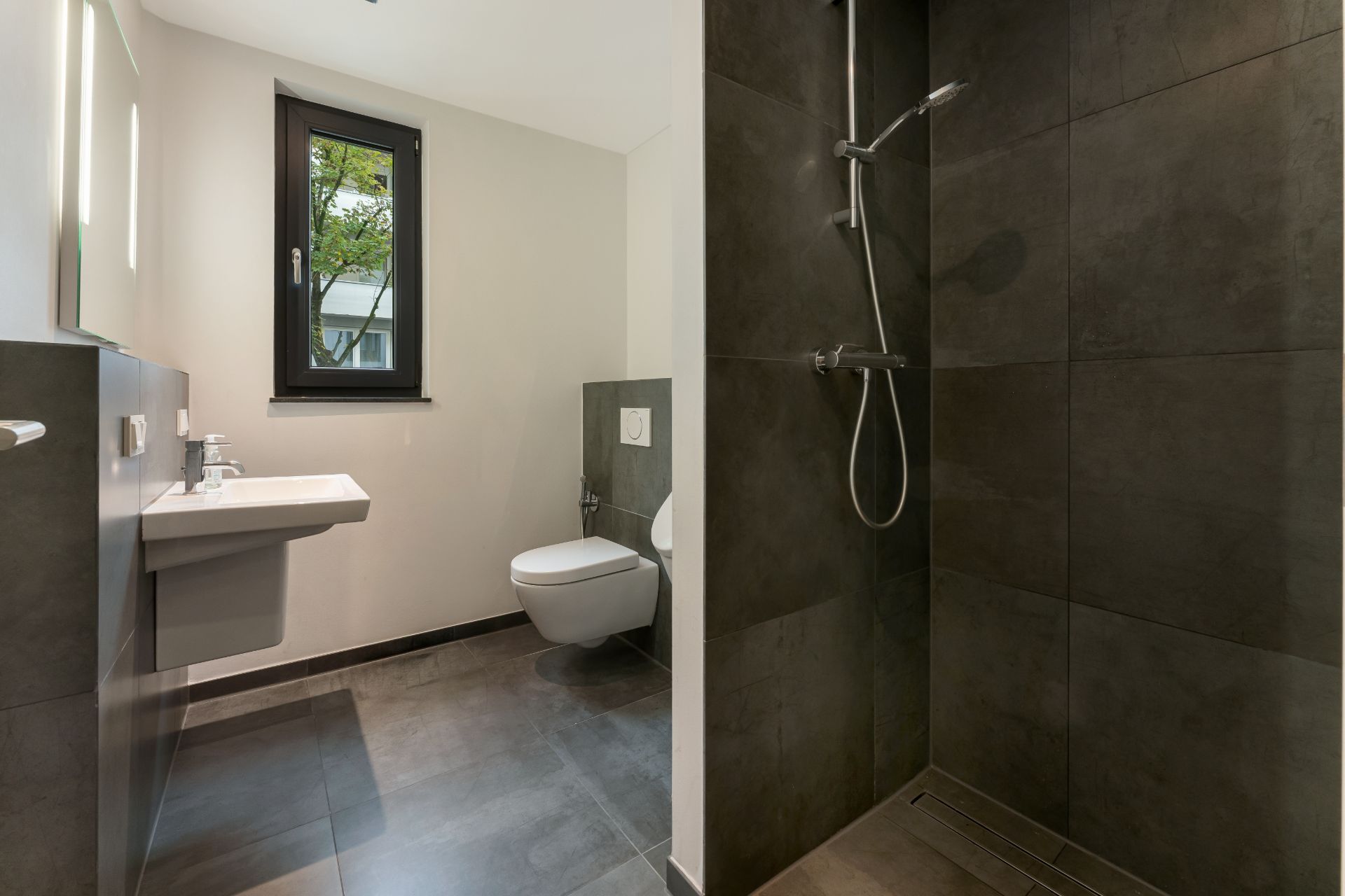 Modernes Badezimmer mit bodengleicher Dusche, Wandwaschbecken, WC und Fenster.