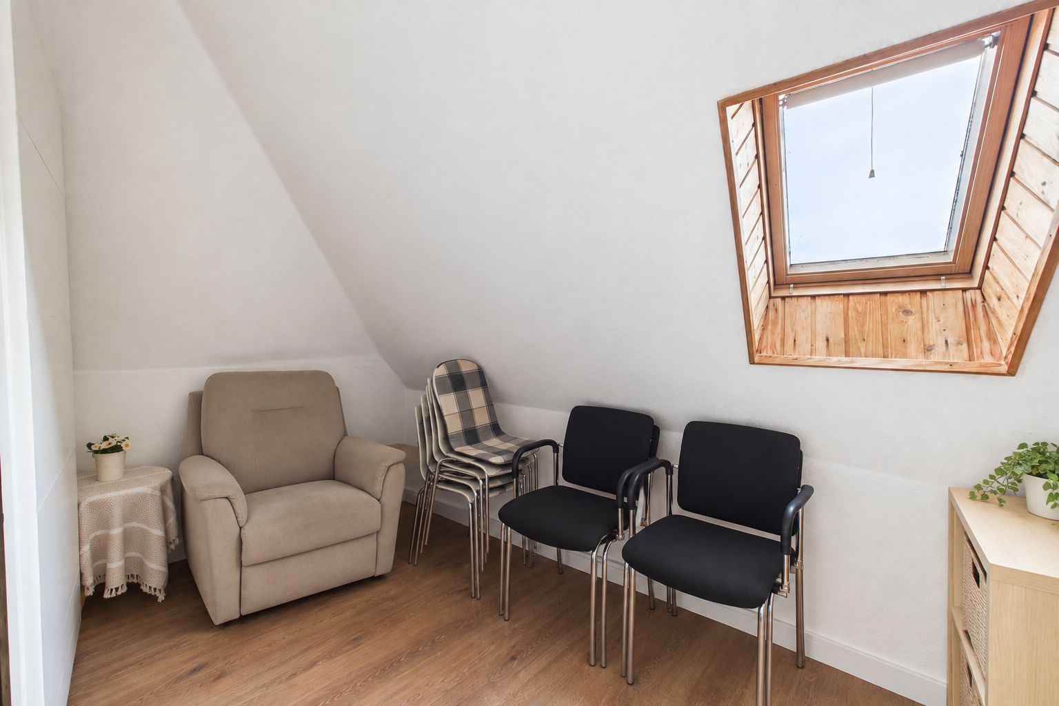 Kleines Zimmer mit Sessel, mehreren Stühlen und Dachfenster, helle Wände und Holzboden.