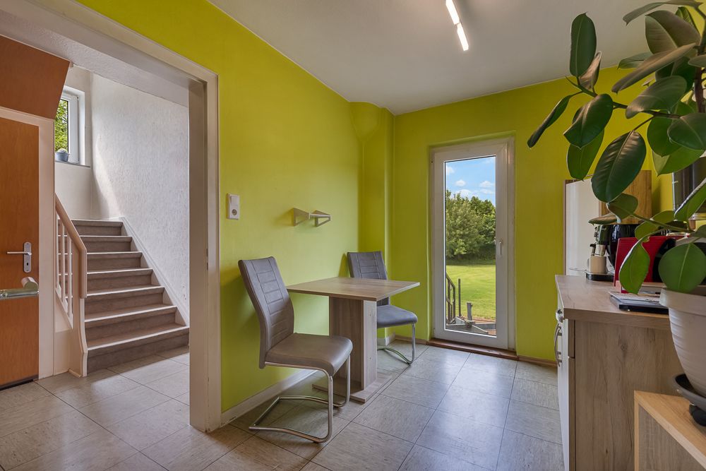 Heller Raum mit gelber Wand, Esstisch, zwei Stühlen, einer Treppe und Zugang zum Garten.