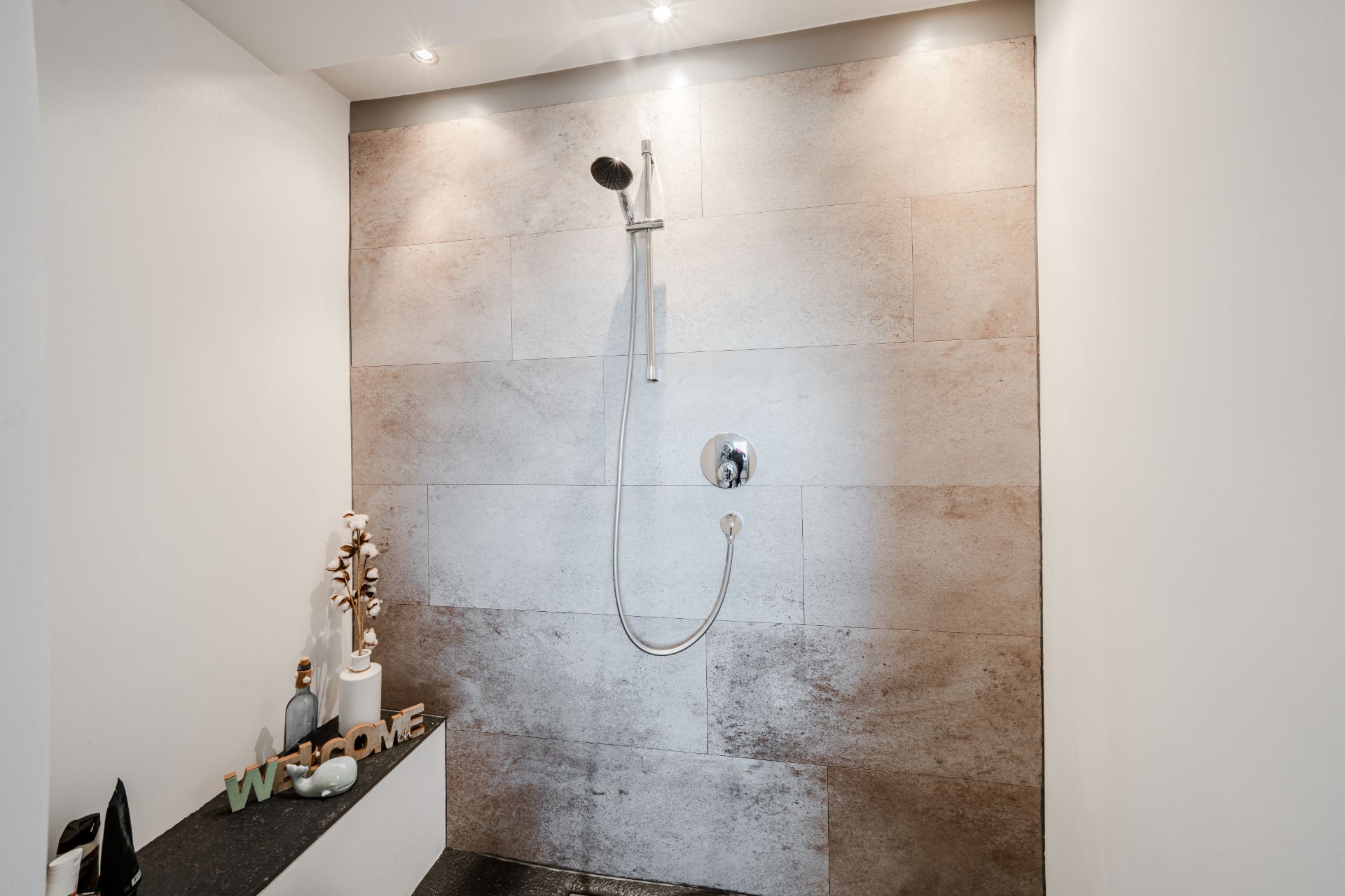 Begehbare Dusche mit heller Fliesenwand und Ablage mit Dekoration.