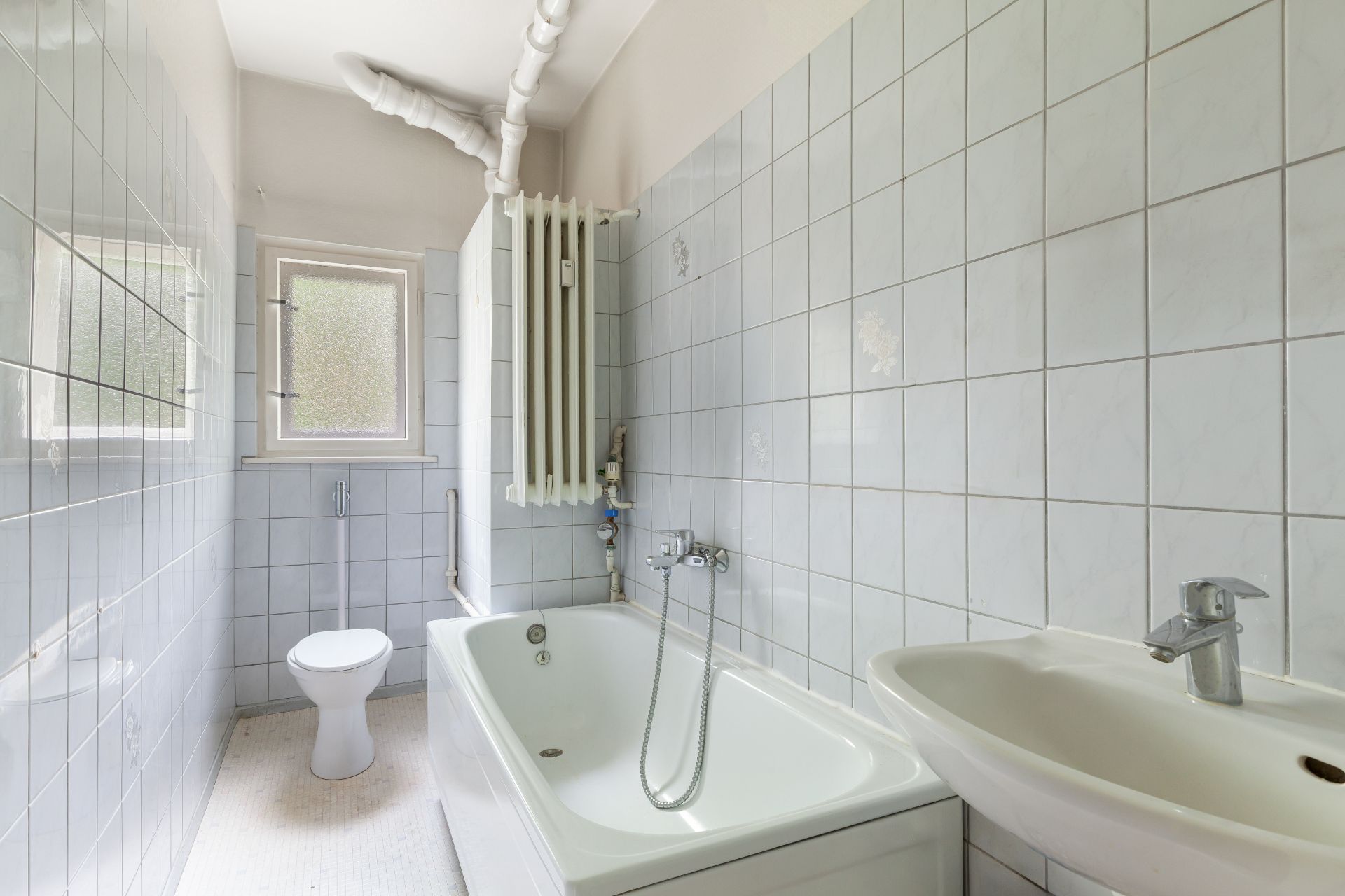 Helles Badezimmer mit Badewanne, Waschbecken, Toilette und Fenster.