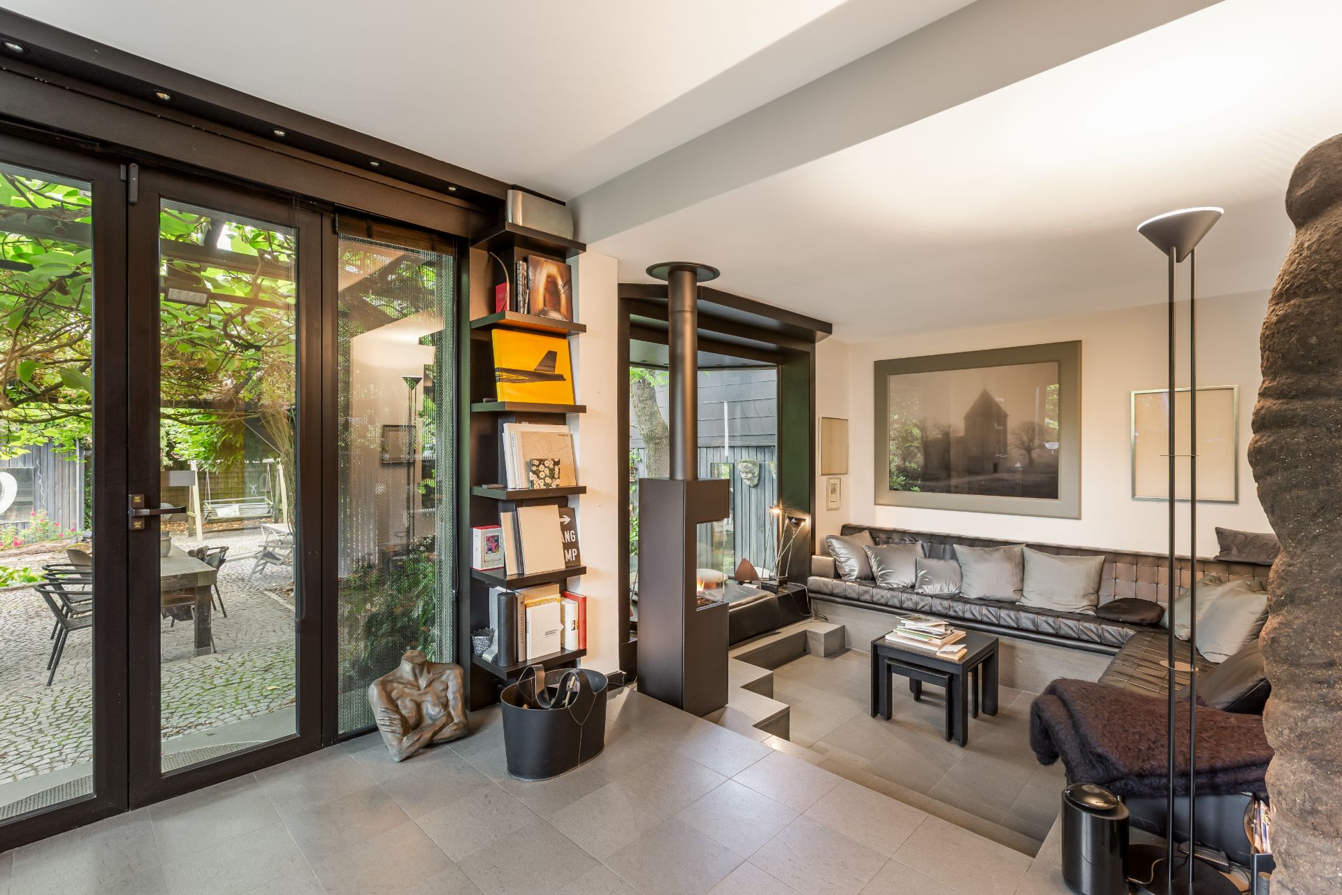 Modernes Wohnzimmer mit großer Glas-Schiebetür, Regal, Sofa und Blick auf Terrasse mit Garten.
