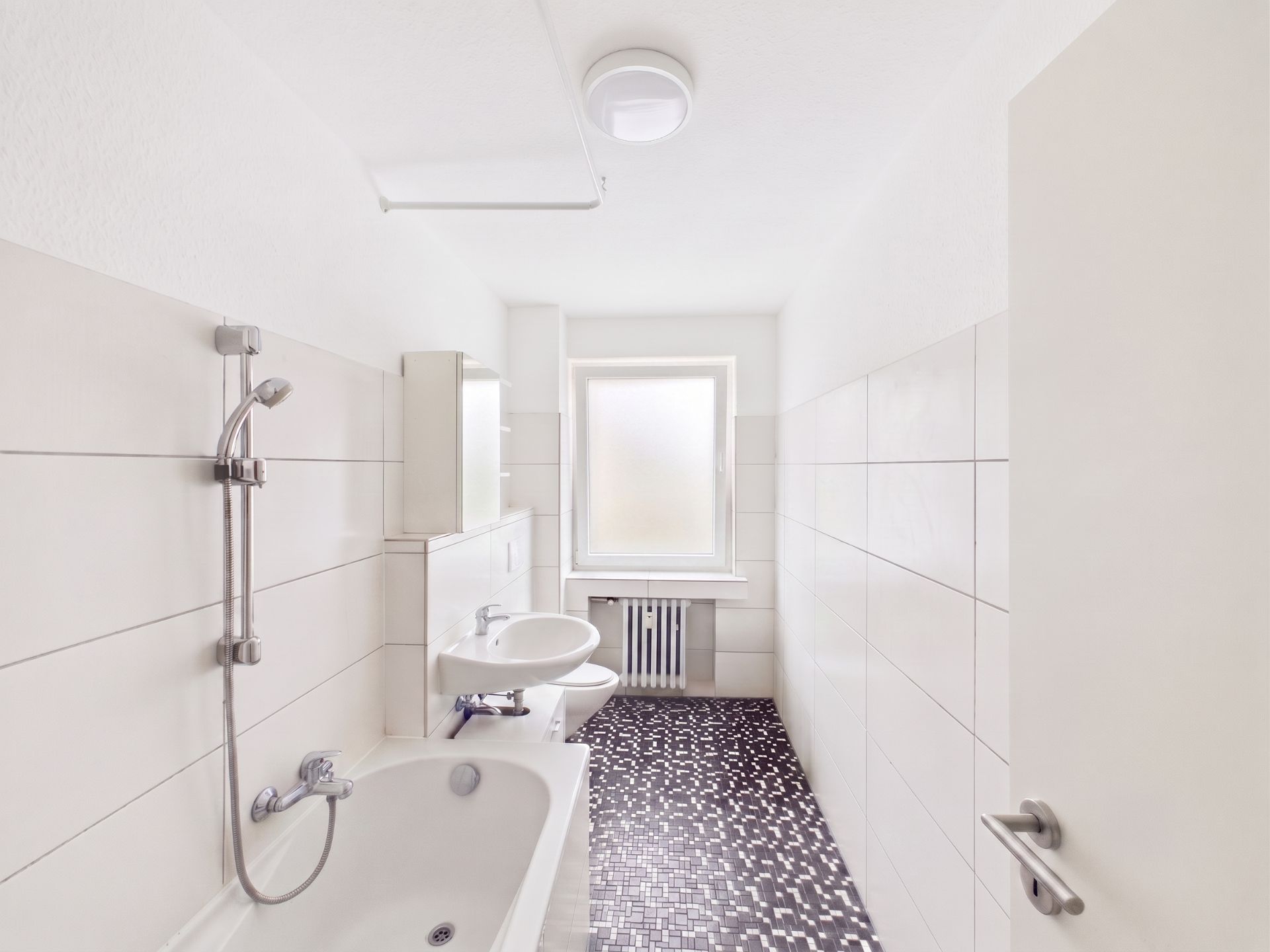 Helles Badezimmer mit Badewanne, Waschbecken, Fenster und schwarz-weißem Fliesenboden.