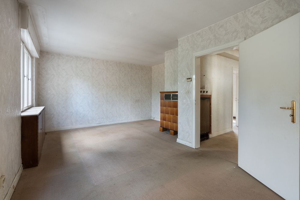 Leeres Wohnzimmer mit Teppichboden, großem Fenster und offen stehender Tür zu einem weiteren Raum.
