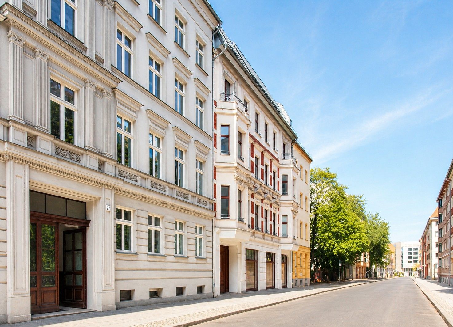 Mehrgeschossiges Wohngebäude mit großen Fenstern an einer ruhigen, baumbestandenen Straße.