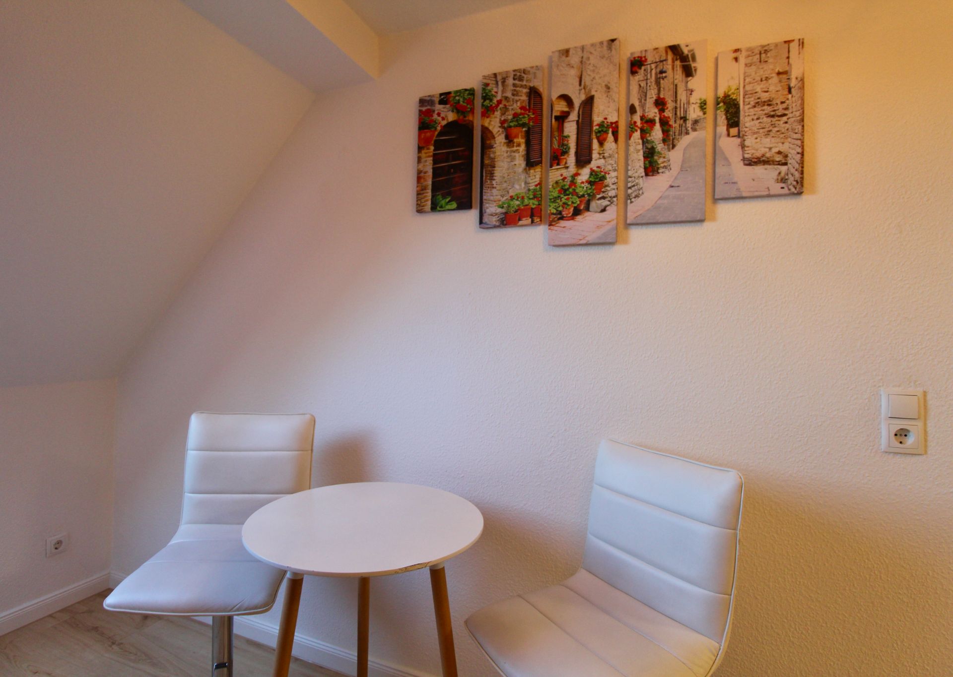 Zwei weiße Stühle und ein runder Tisch vor einer Wand mit Bilddeko.