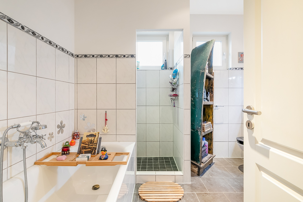 Helles Badezimmer mit Badewanne, Dusche und einem Regal aus einem alten Boot.