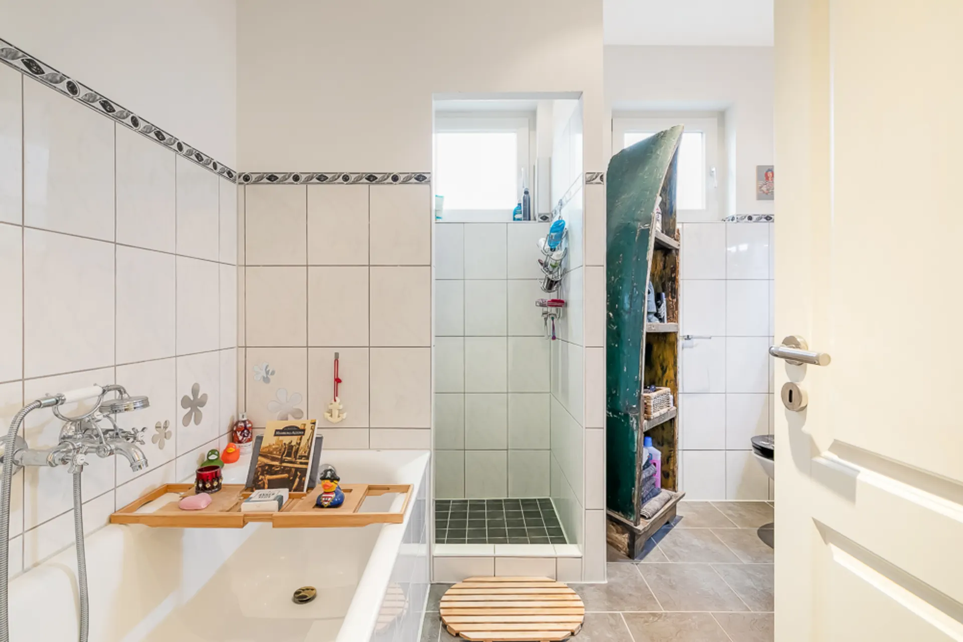 Helles Badezimmer mit Badewanne, Dusche und einem Regal aus einem alten Boot.