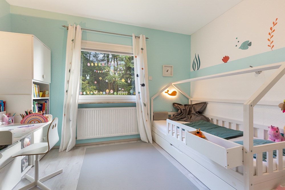 Kinderzimmer mit Hausbett, Schreibtisch, Bücherregal und Fenster mit bunten Aufklebern.