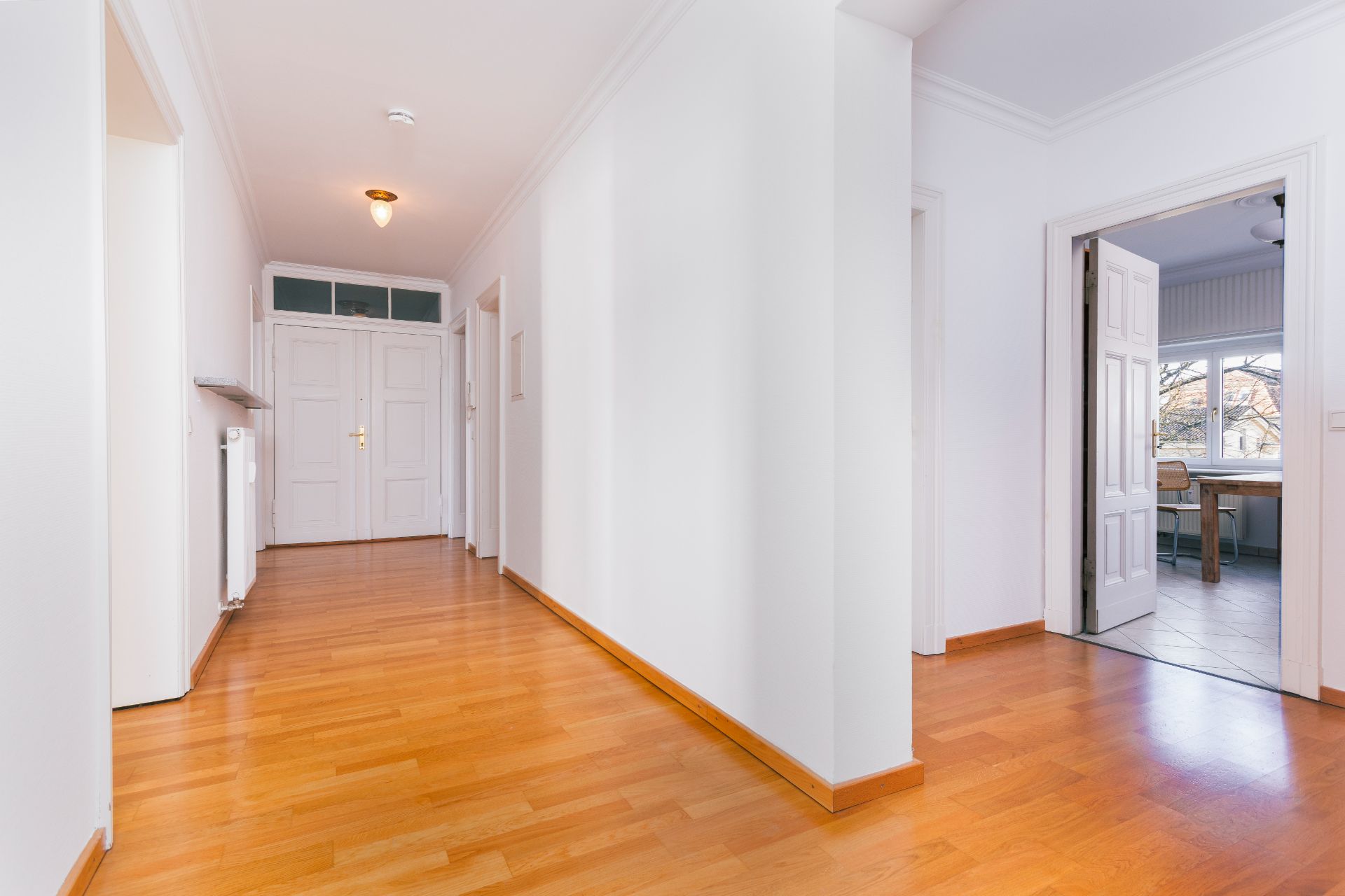 Heller Flur mit Holzfußboden, weißen Wänden und mehreren Türen in einer Wohnung.