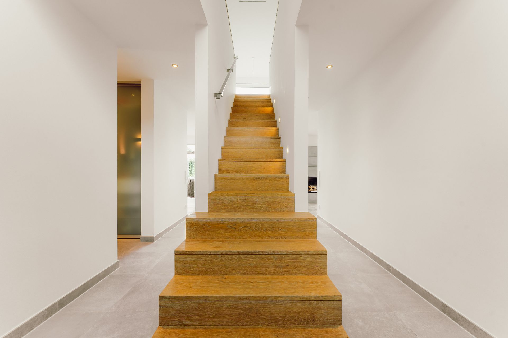 Helle Diele mit breiter, moderner Holztreppe und weißen Wänden.