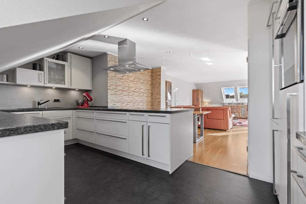 Moderne Einbauküche mit Kücheninsel, offenem Grundriss und Blick ins helle Wohnzimmer.