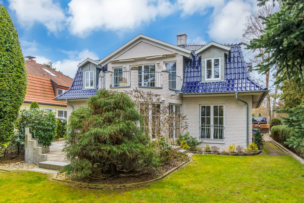 Zweistöckiges Einfamilienhaus mit blauem Dach, großem Fenster und gepflegtem Garten.