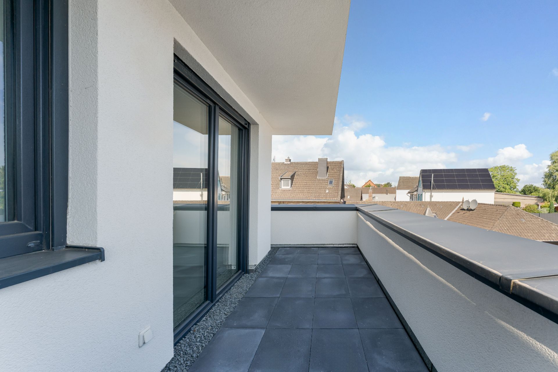 Moderne, überdachte Dachterrasse mit Fliesenboden und Blick auf Nachbarhäuser.