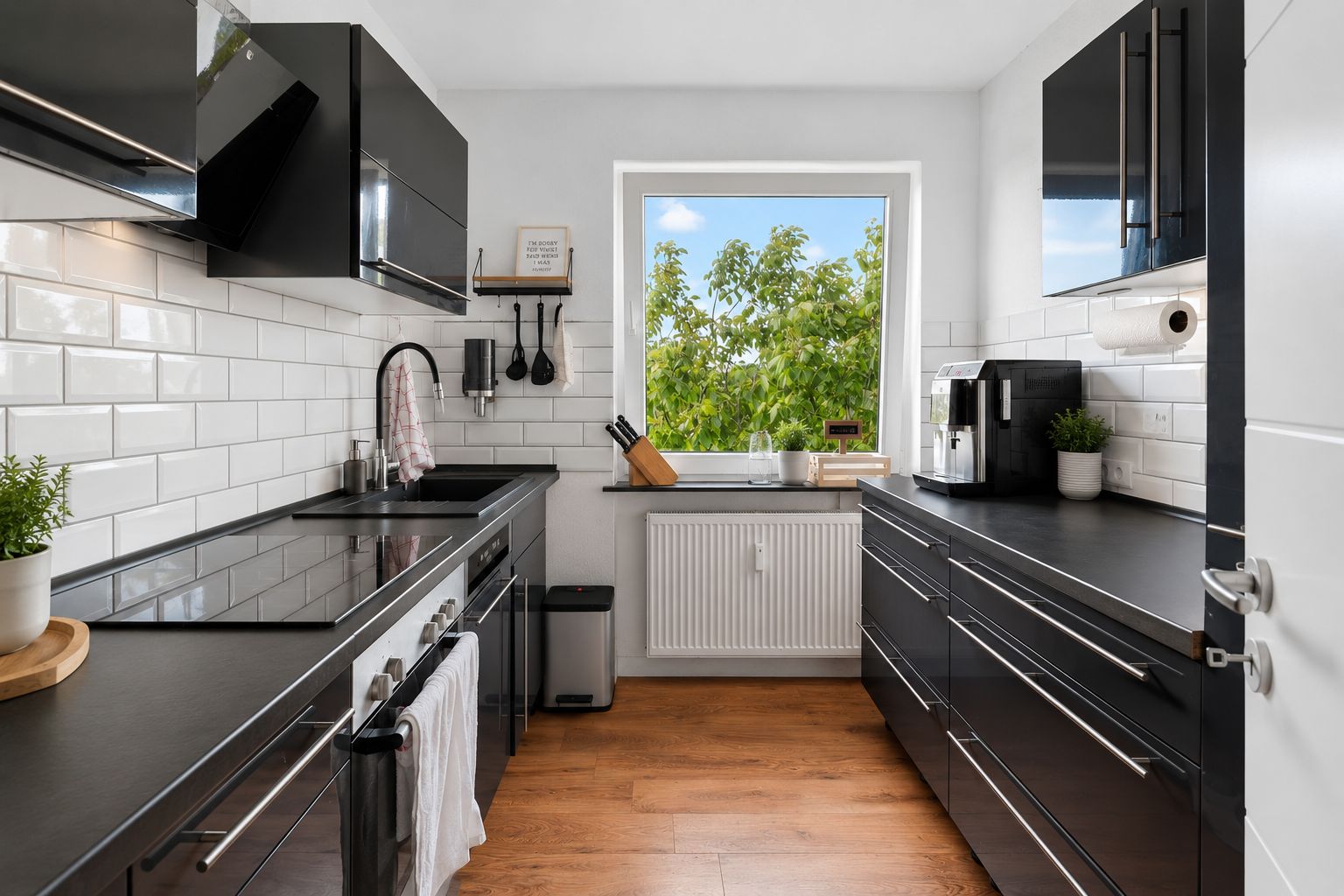 Moderne Küche mit schwarzen Schränken, weißen Fliesen und einem Fenster mit Blick ins Grüne.