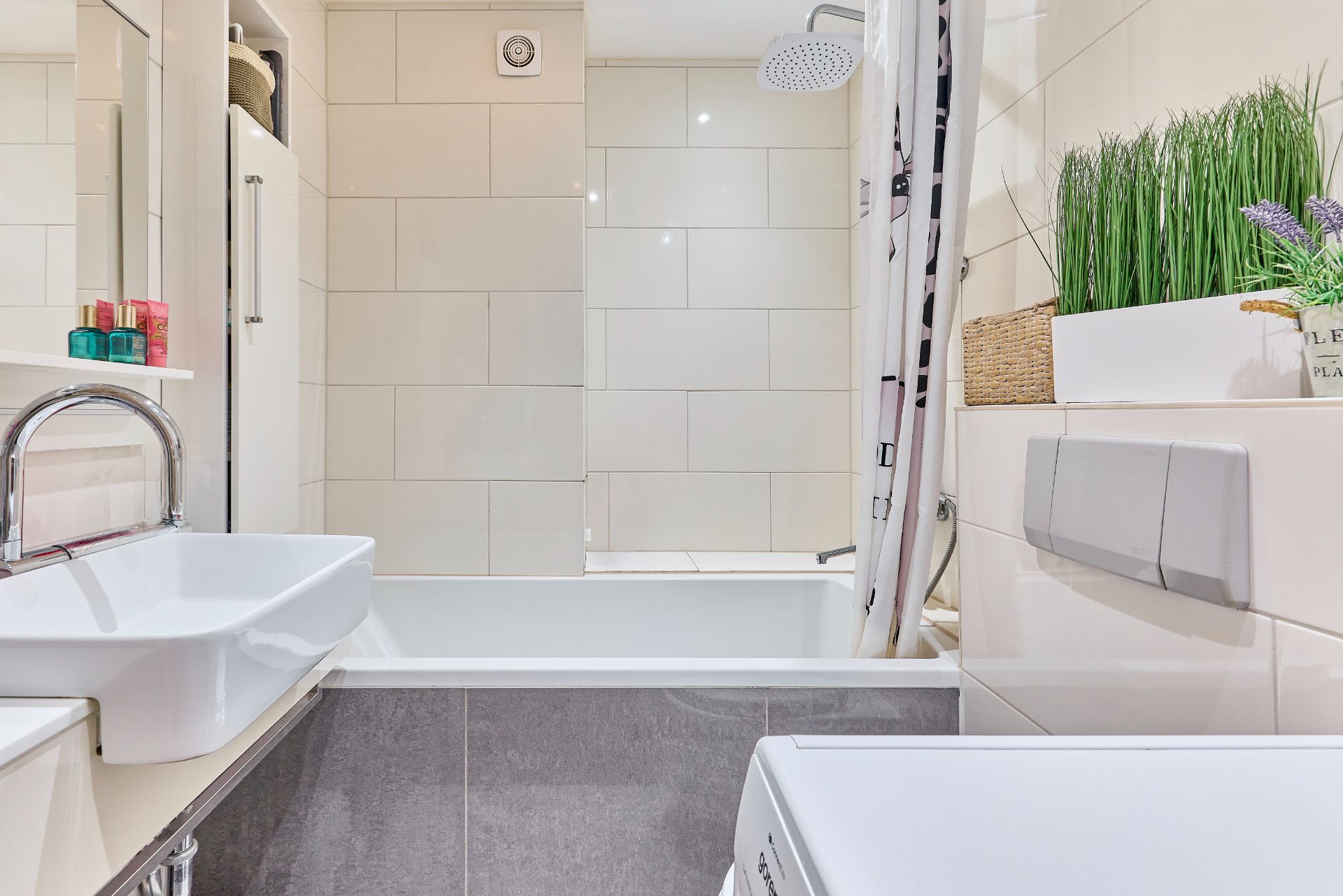 Modernes Badezimmer mit Waschbecken, Badewanne, Dusche, Waschmaschine und Dekopflanzen.