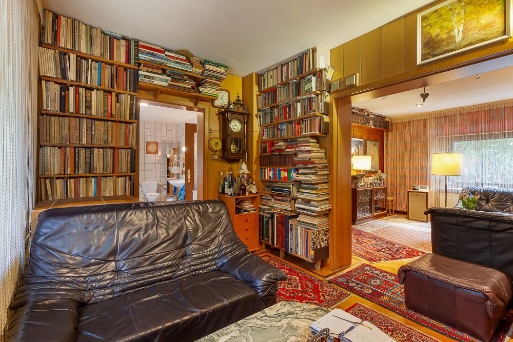 Gemütliches Wohnzimmer mit Ledersofa, vielen Bücherregalen und Blick in ein weiteres Zimmer.