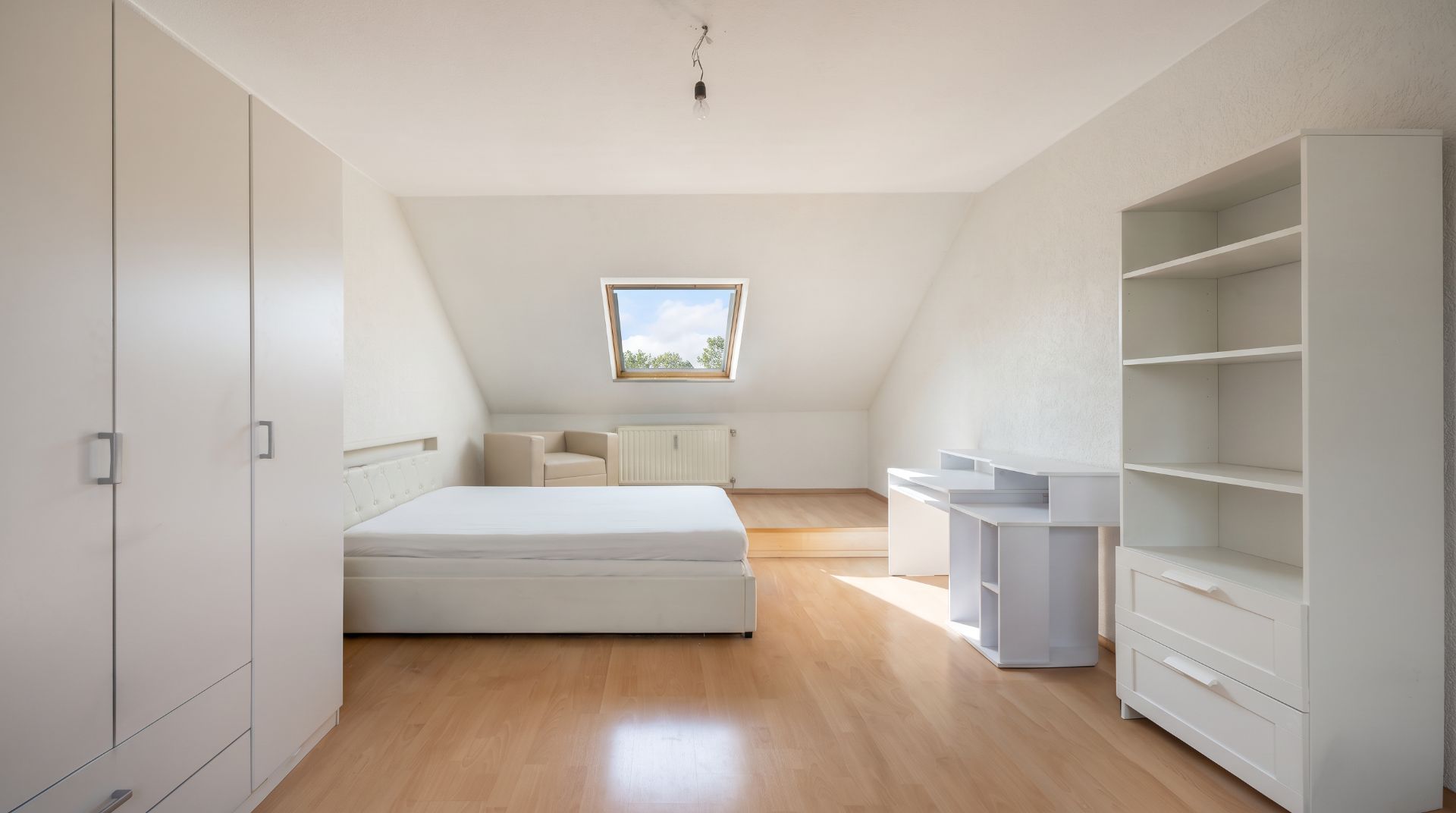 Helles Schlafzimmer mit Bett, Kleiderschrank, Regal, Schreibtisch und Dachfenster.