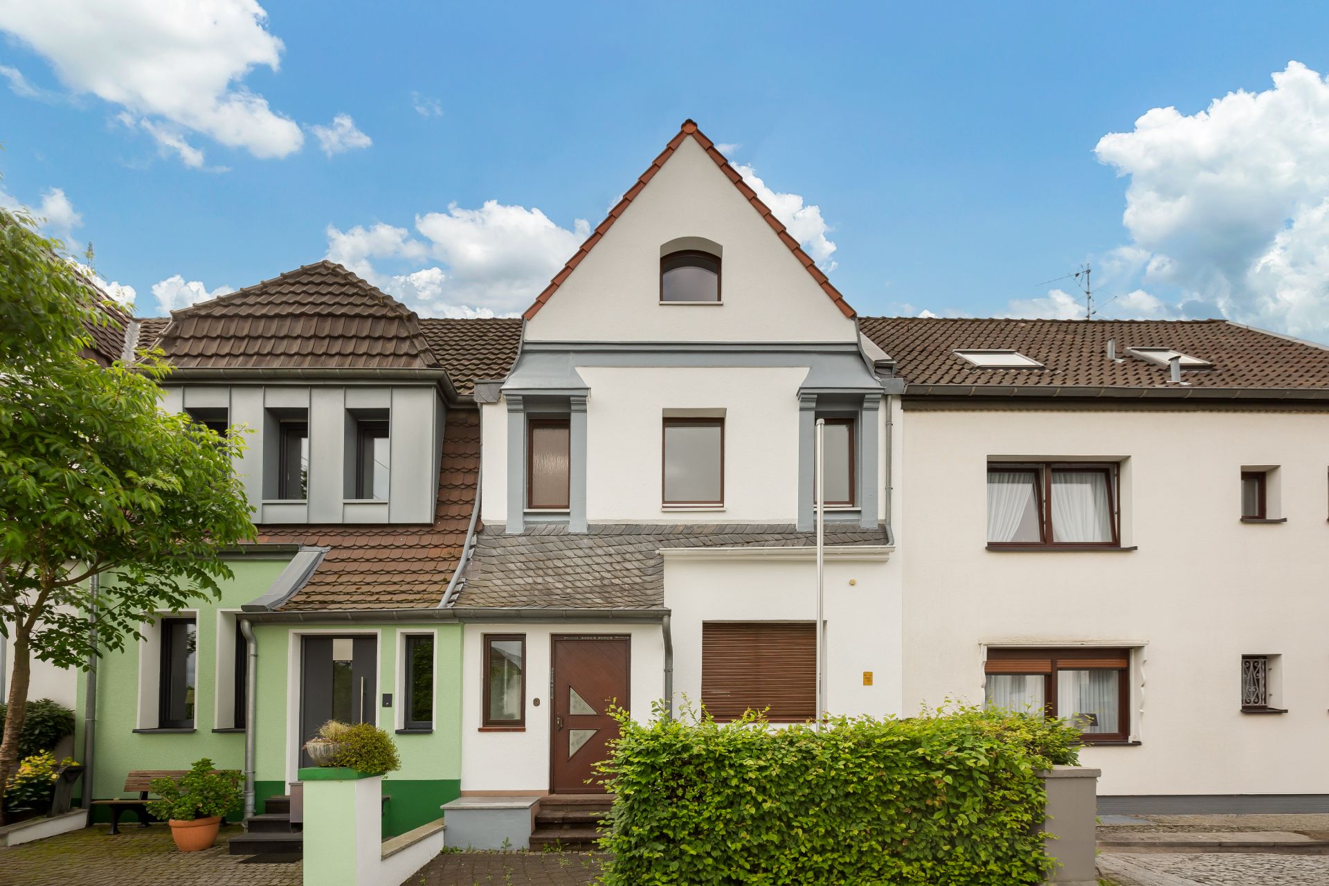 Reihenhaus mit drei Etagen, Vorgarten und grünem Busch vor dem Eingang.