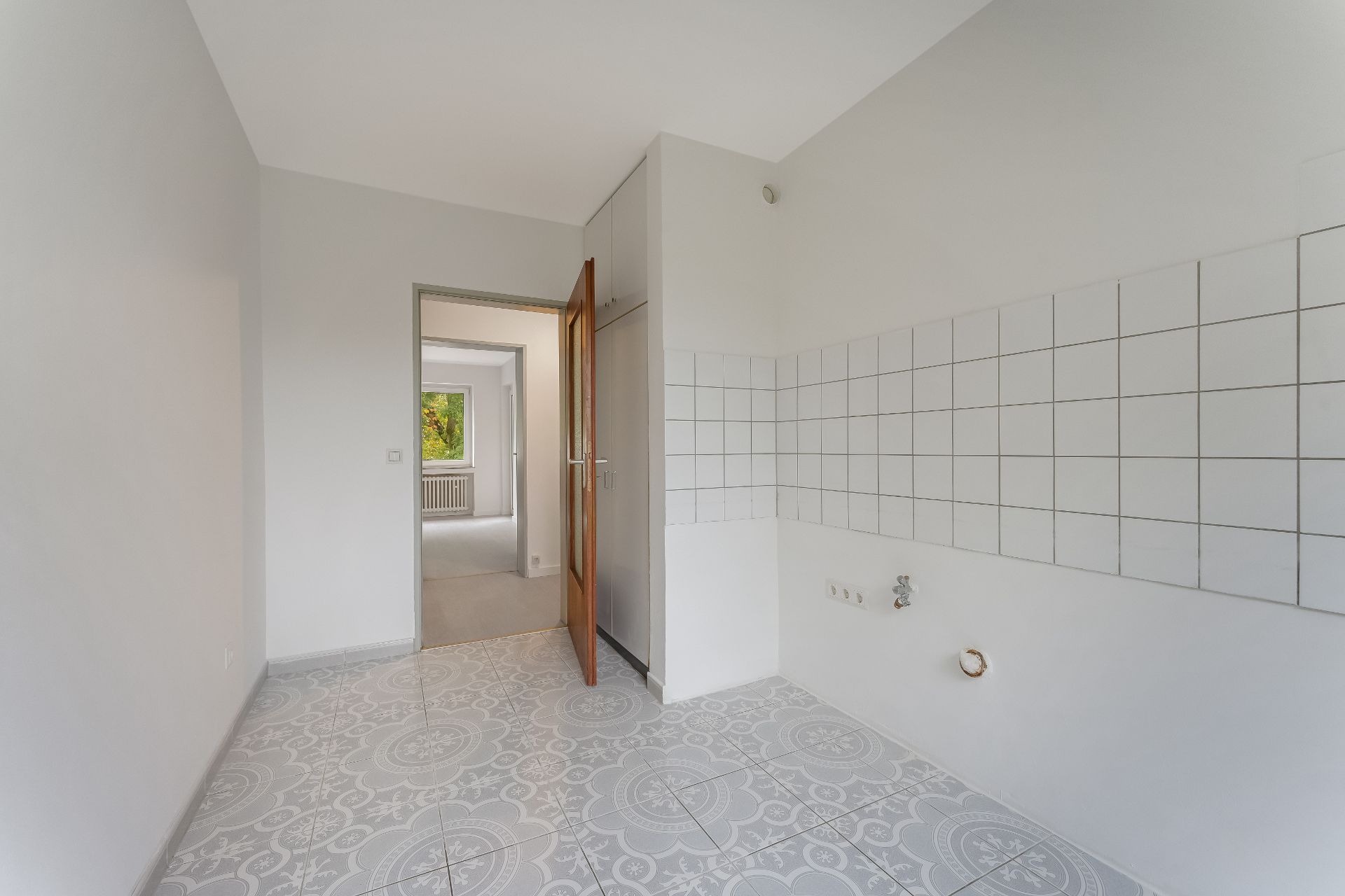 Leerer Raum mit Fliesenboden und weißen Wandfliesen, offene Tür zu weiterem Zimmer.
