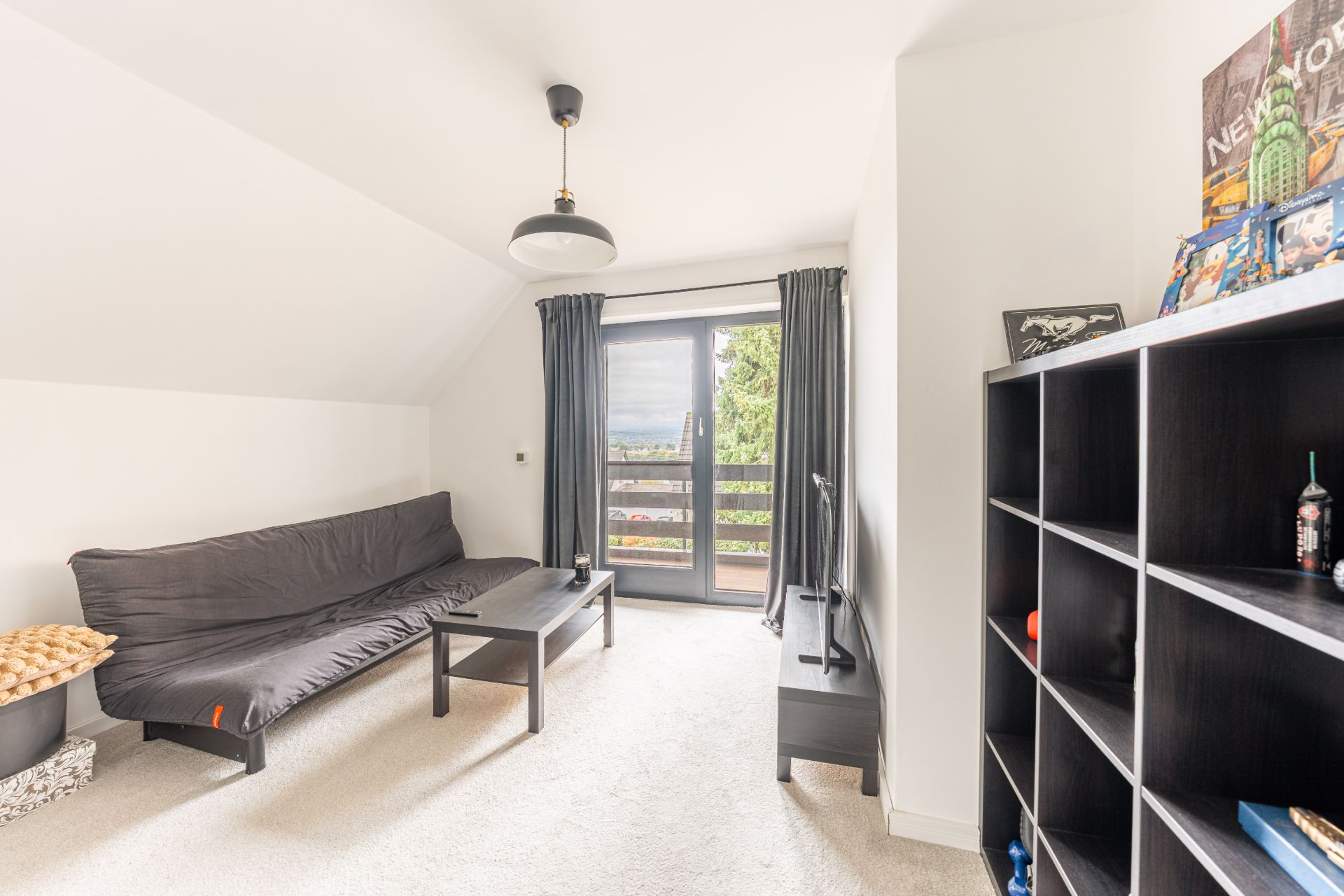 Helles Wohnzimmer mit Sofa, Couchtisch, Regal und Fenster mit Vorhängen und Blick ins Grüne.