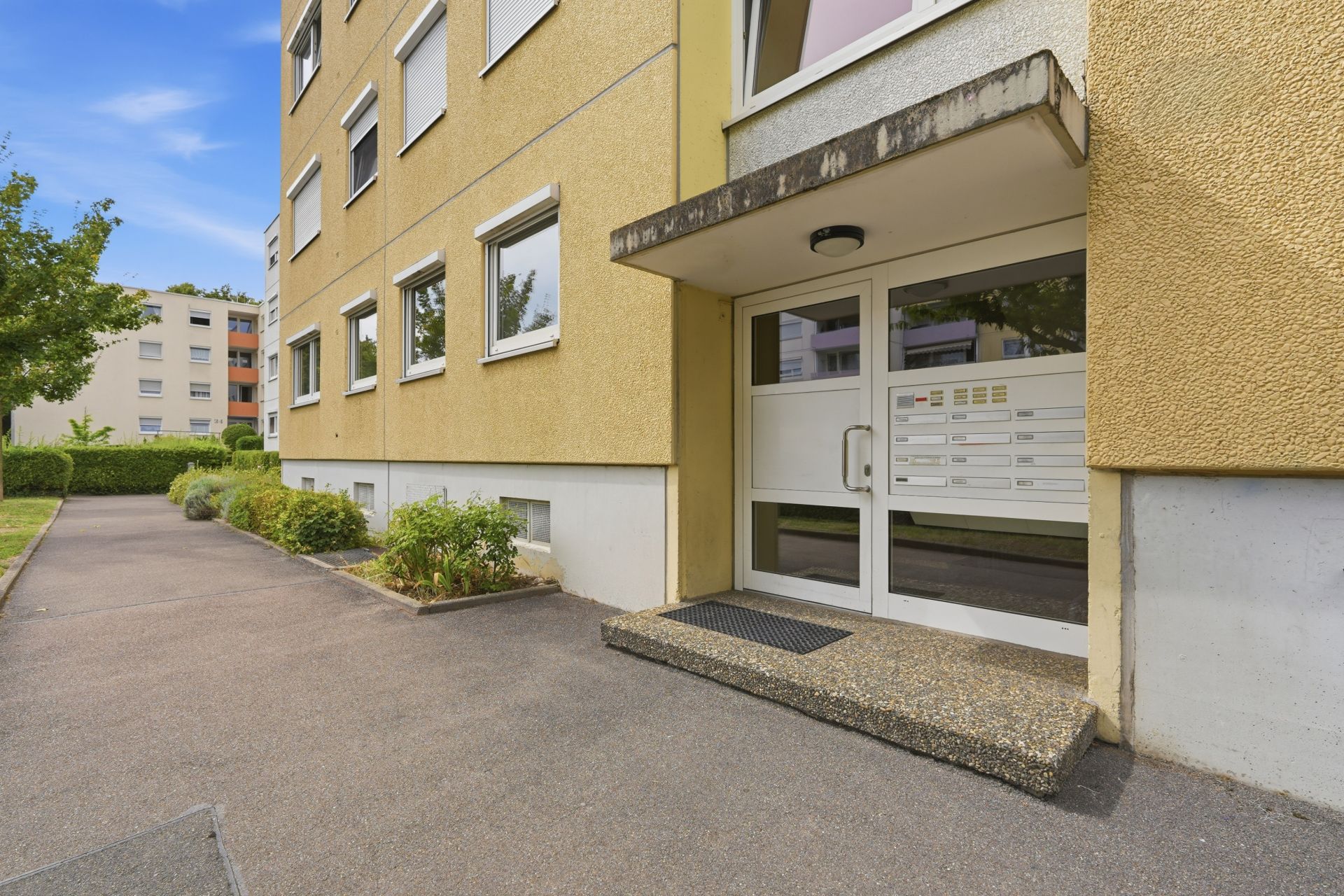 Eingang eines Mehrfamilienhauses mit gelber Fassade und Glas-Eingangstür.