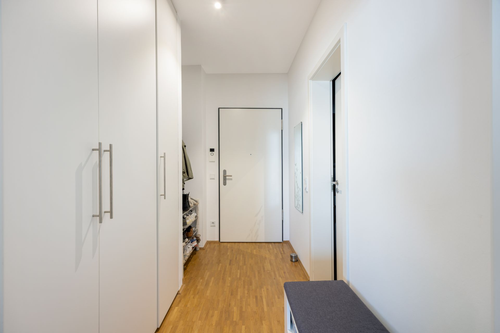 Heller Flur mit Holzfußboden, weißen Wandschränken und einer Eingangstür.