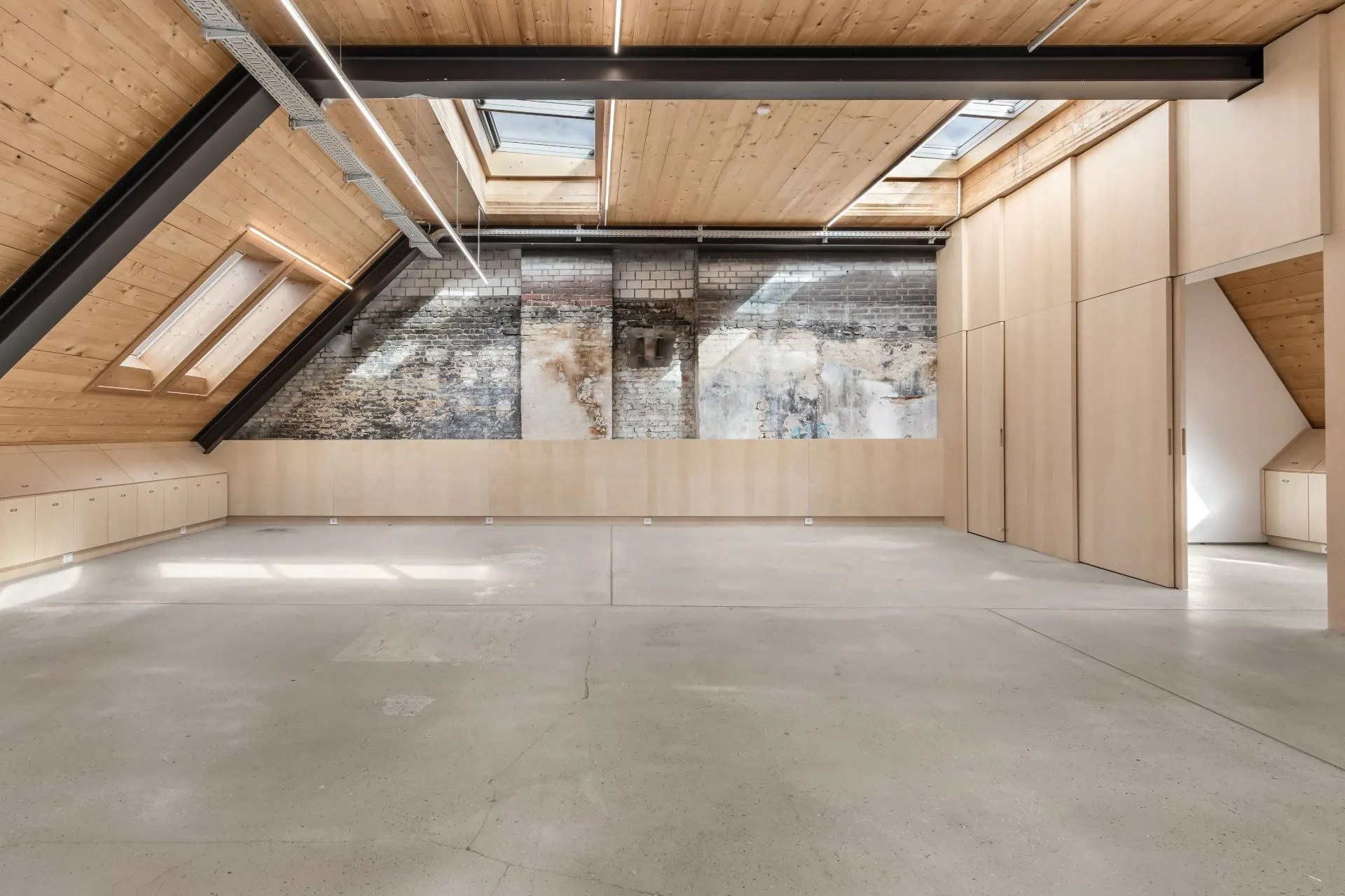 Großer Dachbodenraum mit Holzbalkendecke, Oberlichtern und gemauerter Wand.