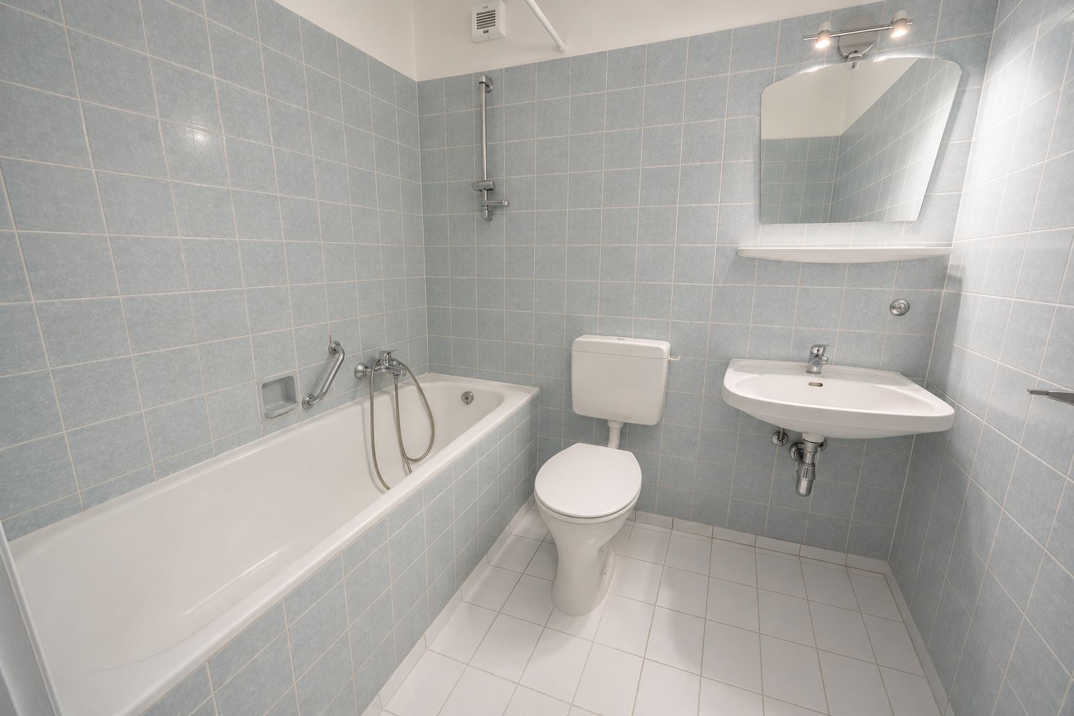 Helles Bad mit Badewanne, WC, Waschbecken und Spiegel, Wände und Boden sind gefliest.