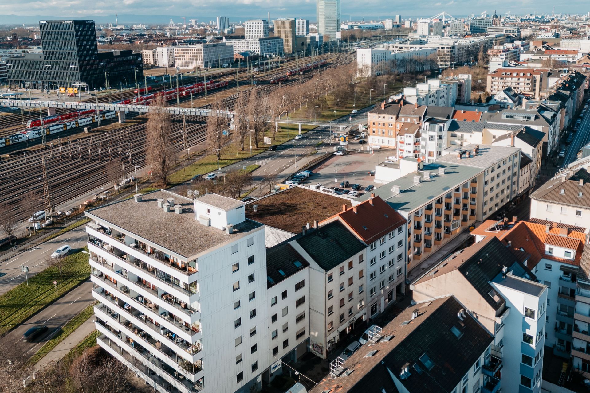 Luftaufnahme von Wohngebäuden an einer Straße mit Bahngleisen im Hintergrund.