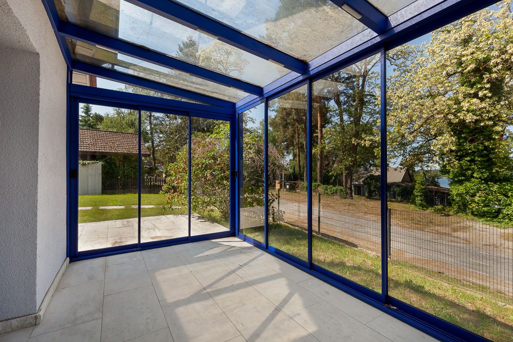 Wintergarten mit blauen Rahmen und großen Glasfenstern, Blick ins Grüne.