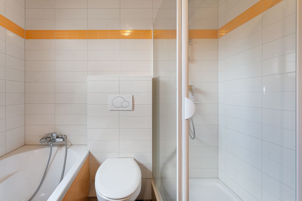 Modernes Badezimmer mit Badewanne, Toilette und separater Dusche mit orangem Fliesenstreifen.