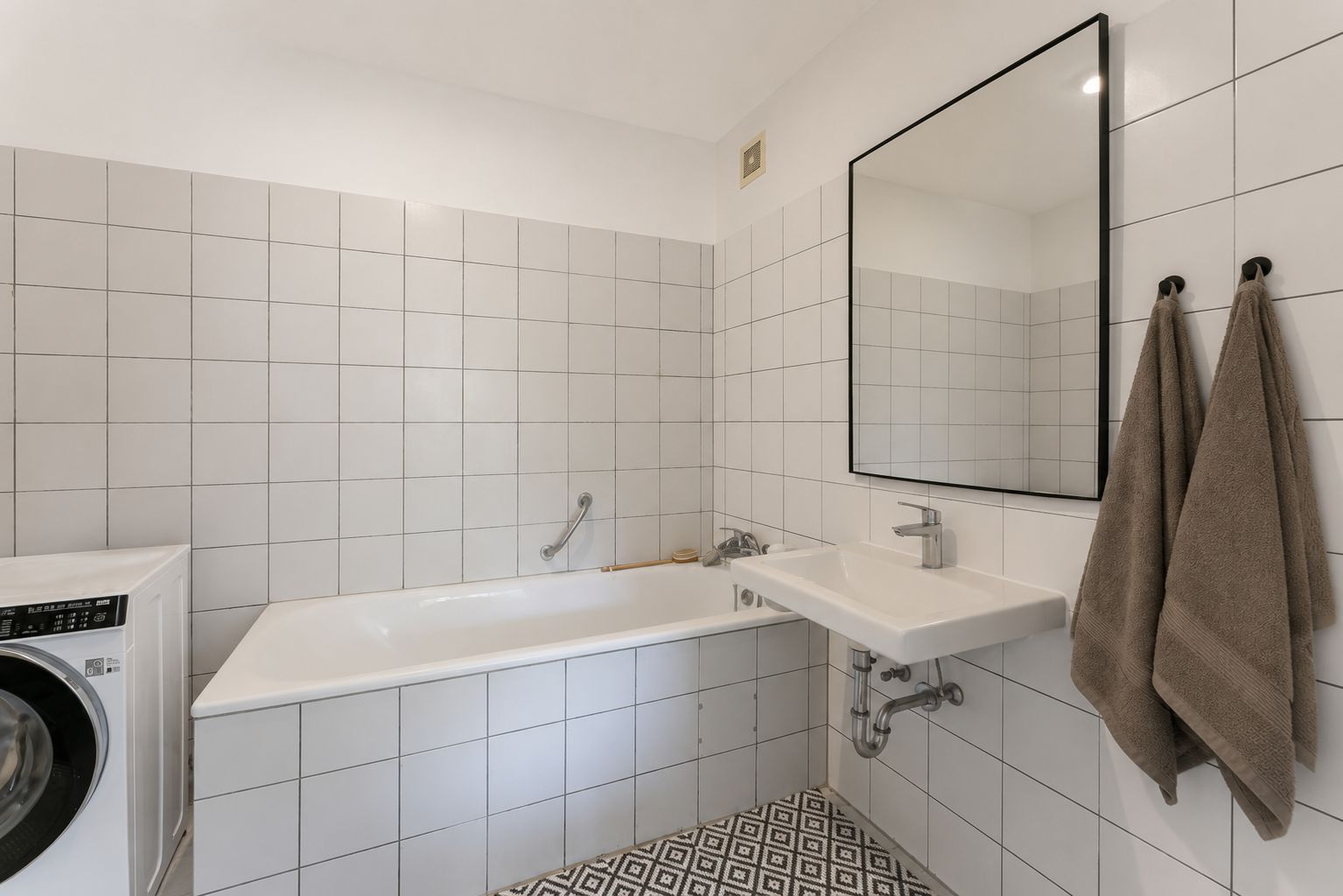 Helles Bad mit Badewanne, Waschbecken, großem Spiegel und zwei Handtüchern an der Wand.