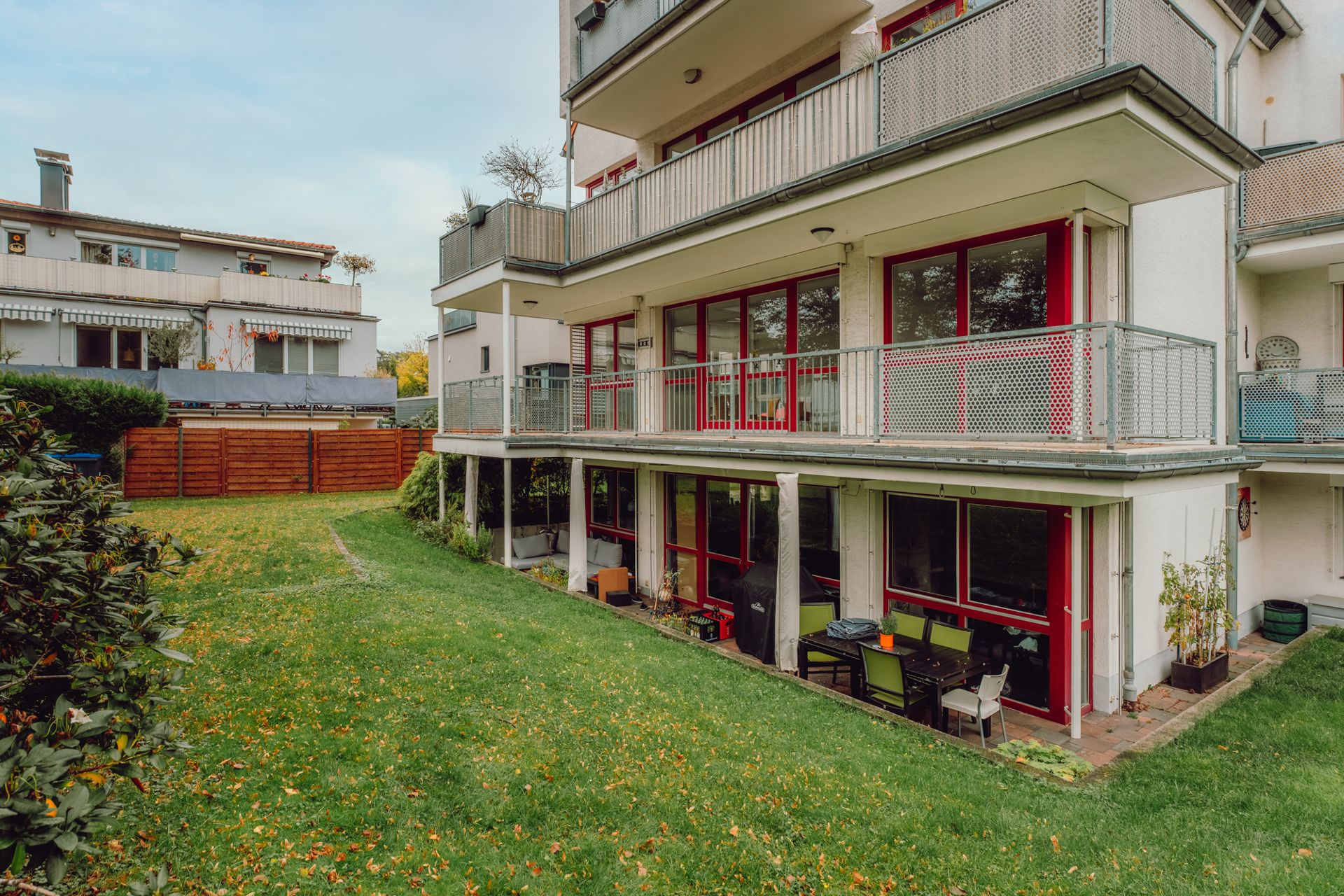 Mehrfamilienhaus mit Balkonen und Garten, Blick auf Terrasse mit Sitzmöbeln.
