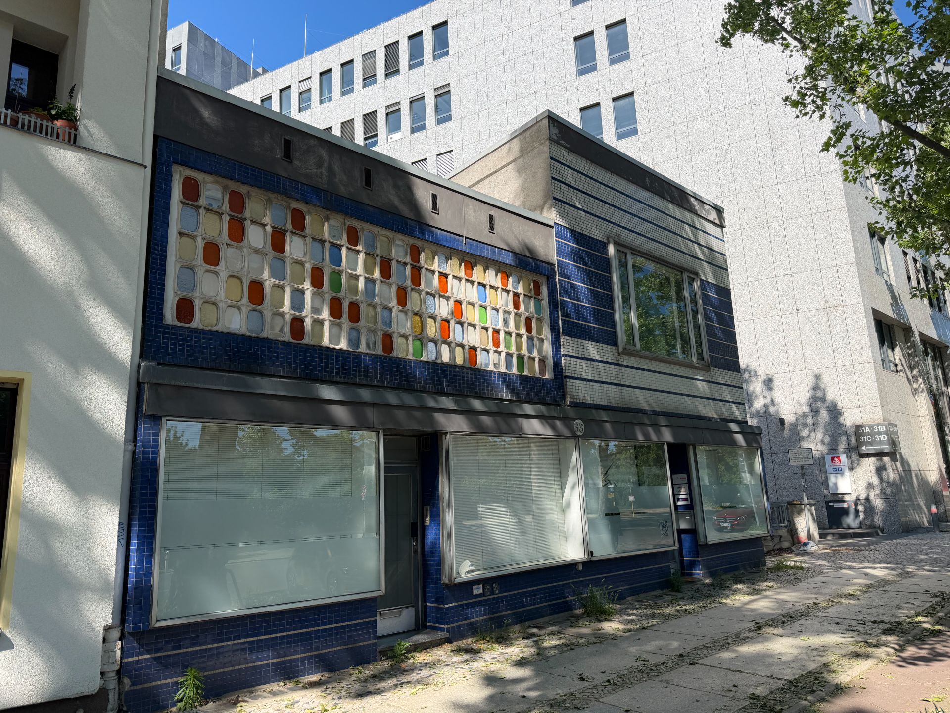 Zweistöckiges Gebäude mit blauen Fliesen und bunten Glasbausteinen über den Fenstern.