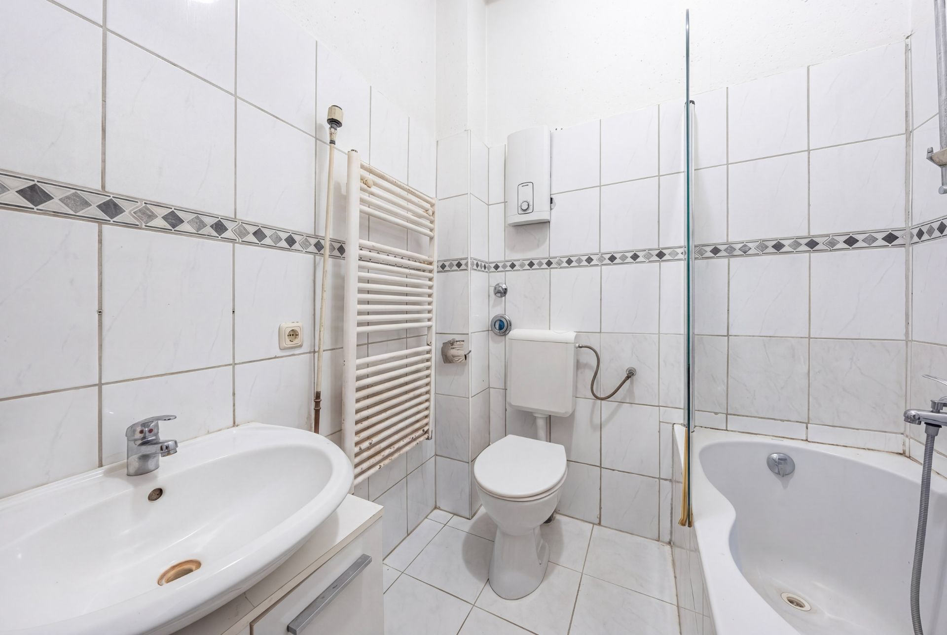 Helles Badezimmer mit Waschbecken, Toilette, Badewanne und Handtuchheizkörper.