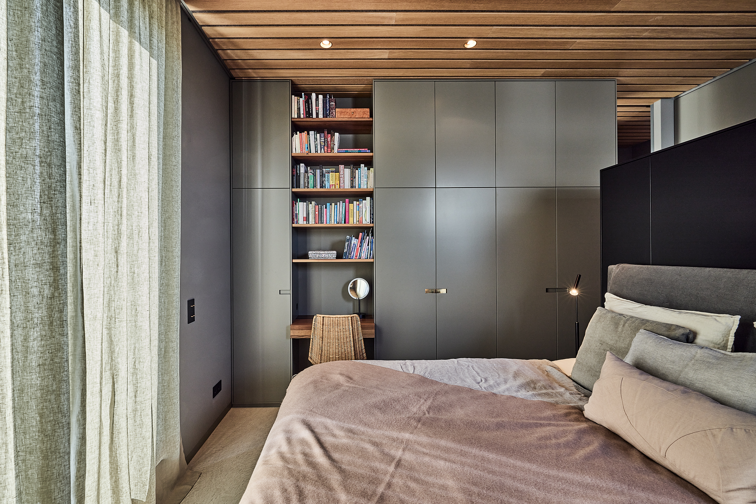 Modernes Schlafzimmer mit großem Bett, grauen Schränken, Bücherregal und kleinem Schreibtisch mit Stuhl.