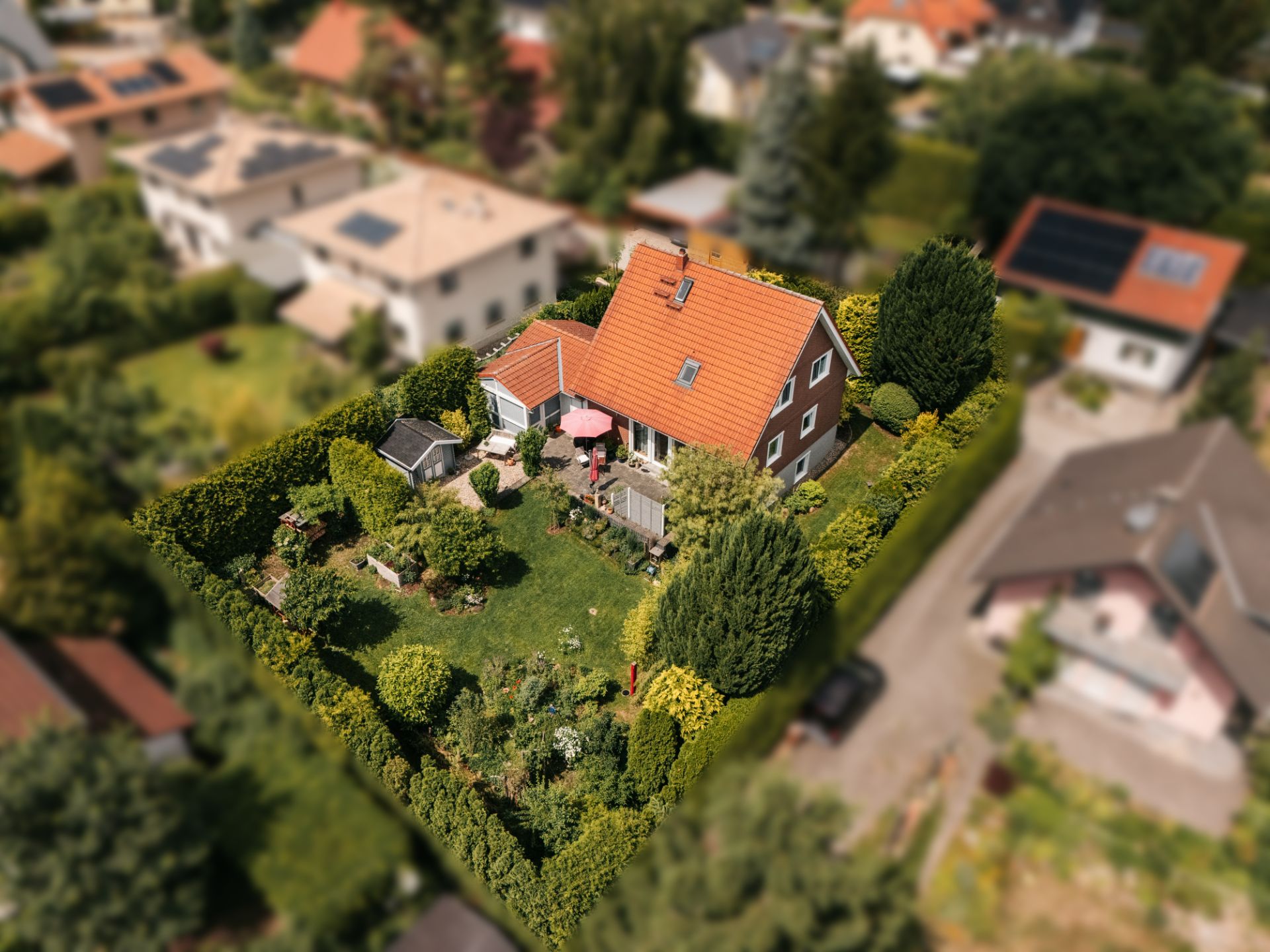 Luftaufnahme eines Einfamilienhauses mit rotem Dach und großem, grünen Garten.