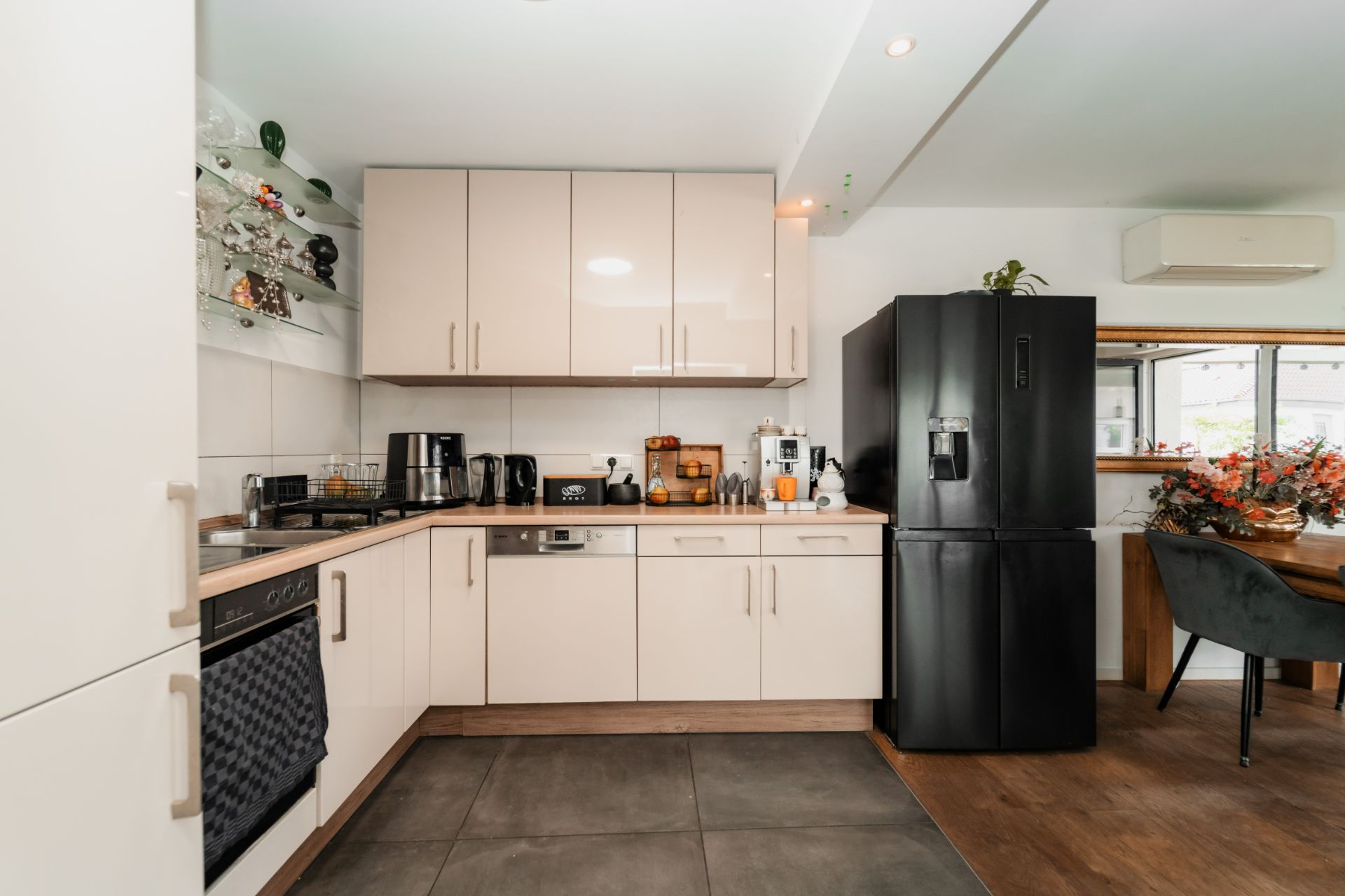 Moderne Küche mit weißen Schränken, schwarzem Kühlschrank und Geräten auf der Arbeitsplatte.