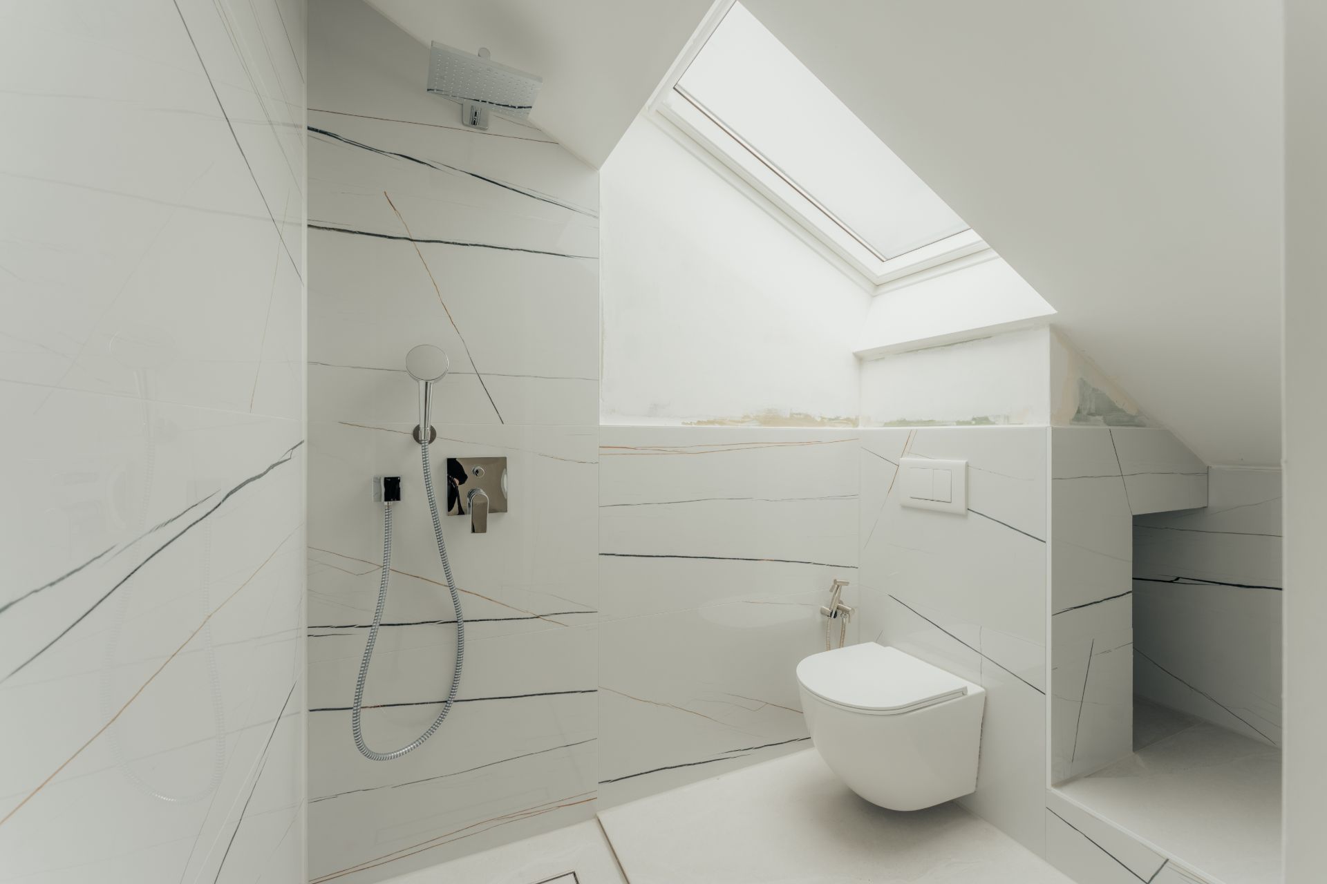 Helles Bad mit Dusche, Toilette und Dachfenster unter einer Schräge.