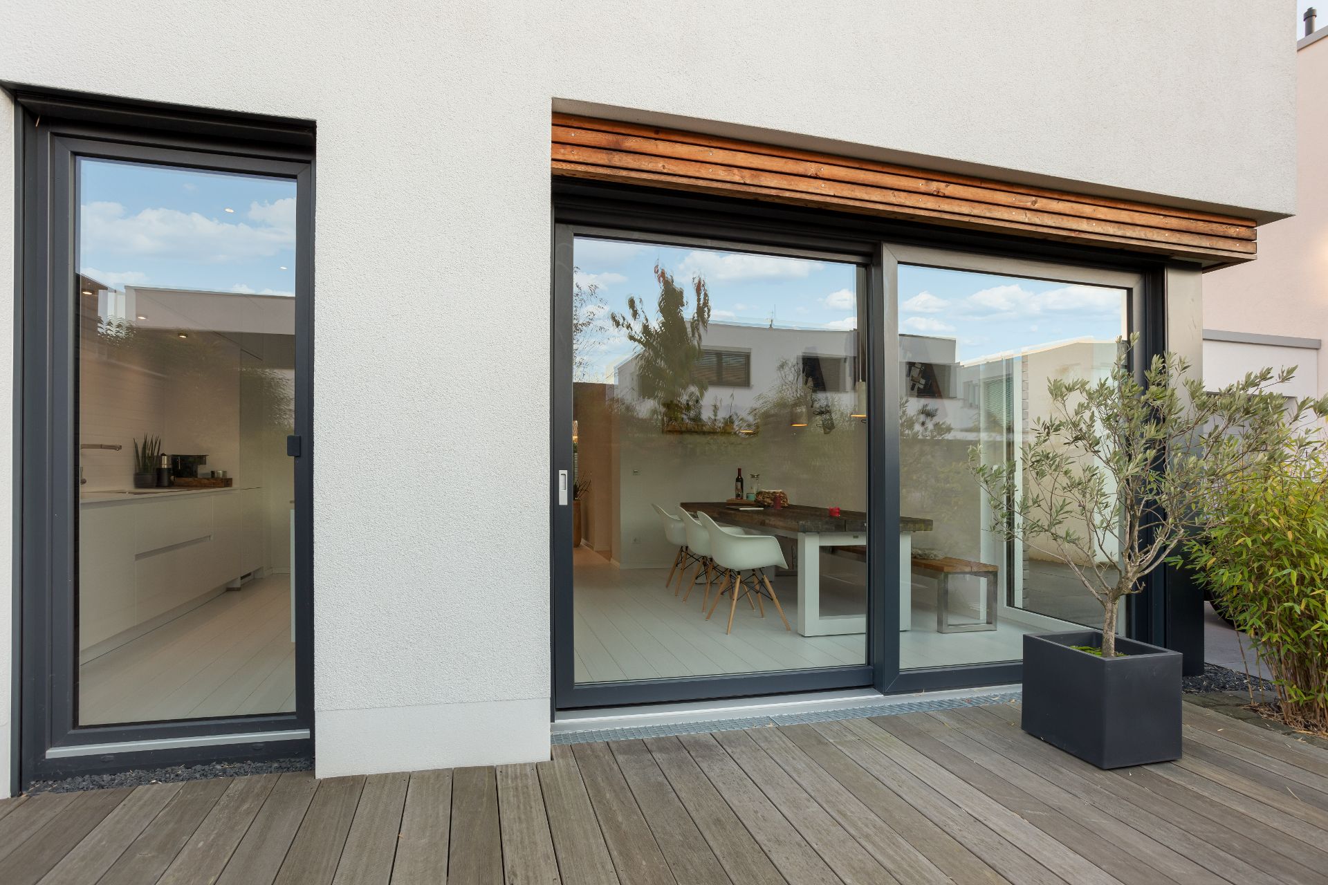 Moderne Terrasse mit Holzboden, großen Fenstern und Blick auf Essbereich und Küche.