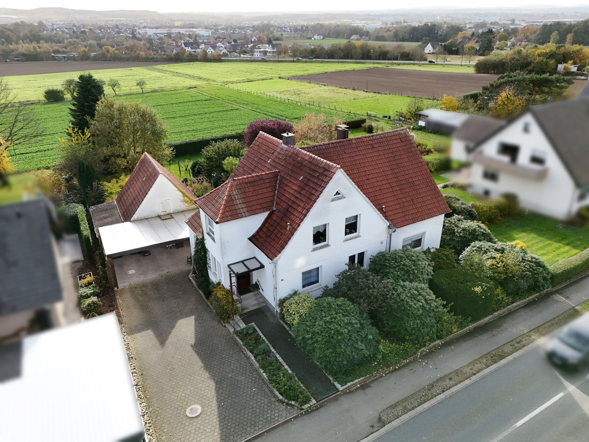 Weißes Einfamilienhaus mit rotem Dach, Vorgarten und Carport, umgeben von viel Grün.