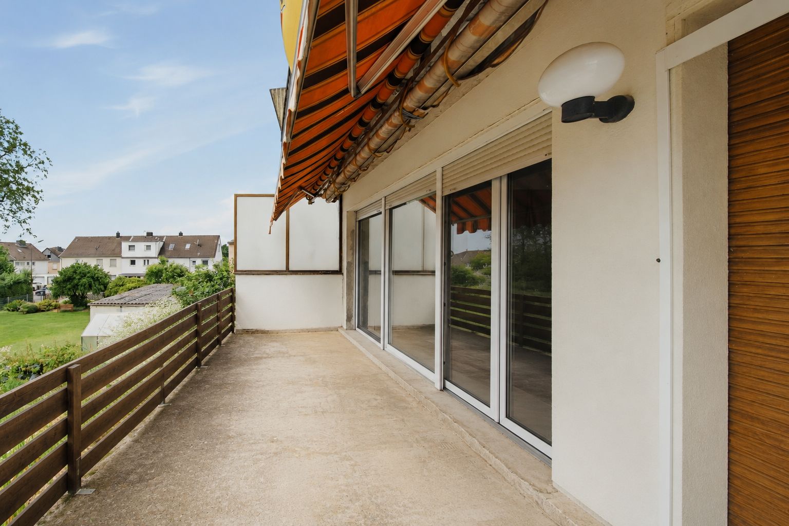 Großer Balkon mit Markise, Holzzaun und Blick auf Garten und Nachbarhäuser.