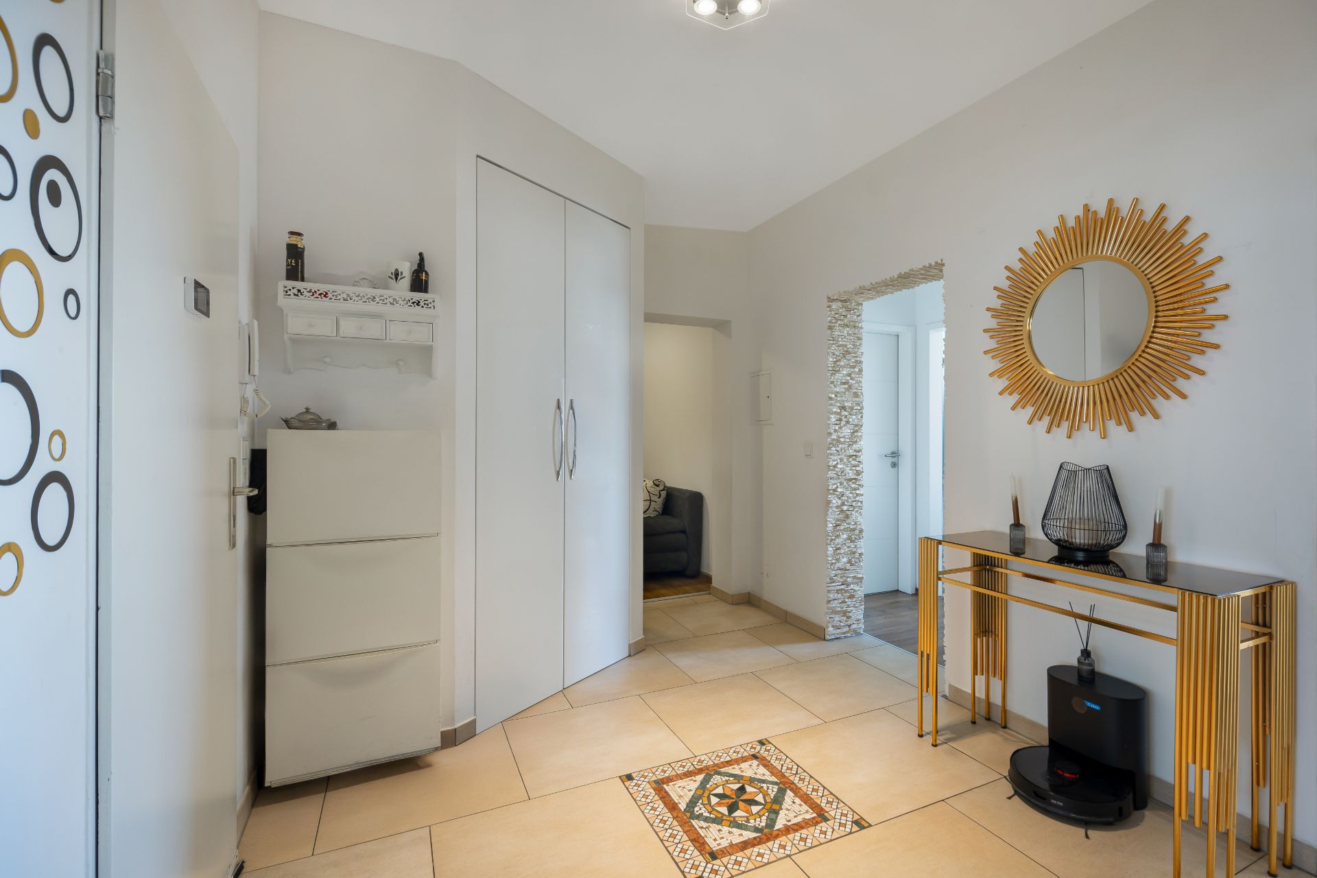 Heller Flur mit Wandspiegel, Kommode, Garderobe und Fliesenmuster auf dem Boden.