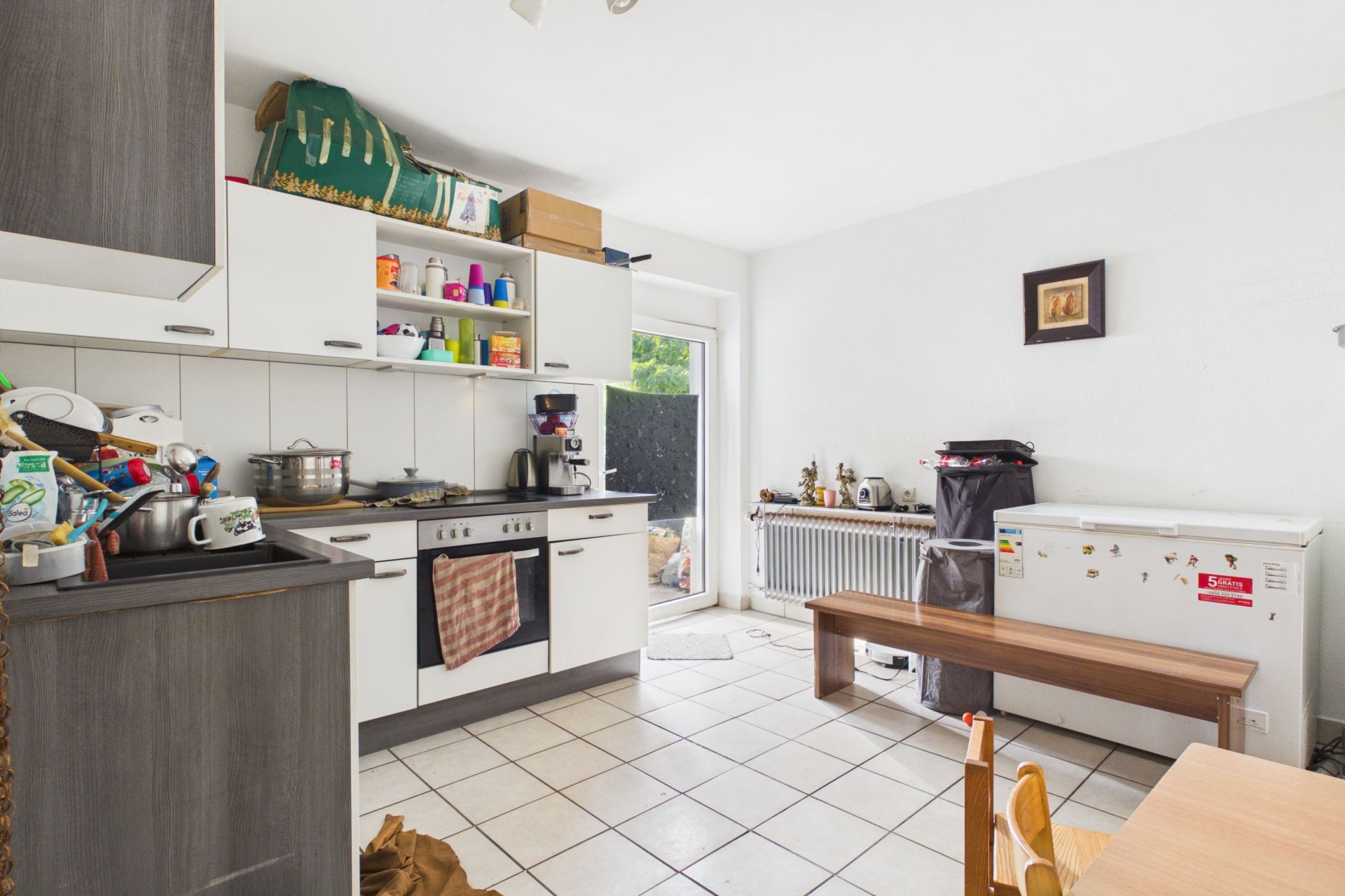 Helle Küche mit Herd, Gefrierschrank, Holzbank und Tür zum Garten.