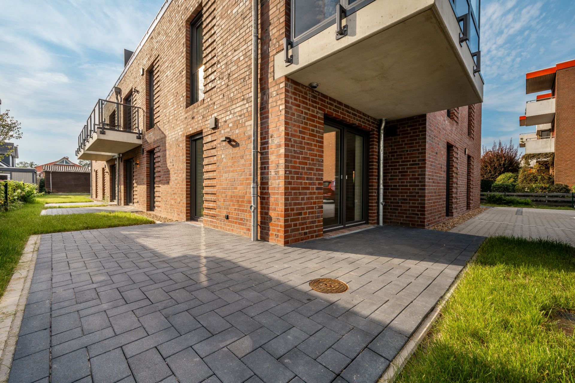 Erdgeschoss eines modernen Backsteinhauses mit Terrasse und Rasenflächen.