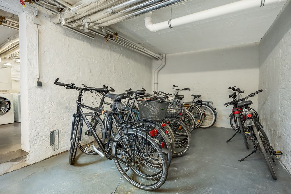 Fahrräder stehen in einem Kellerraum mit weißen Wänden und sichtbaren Rohren.