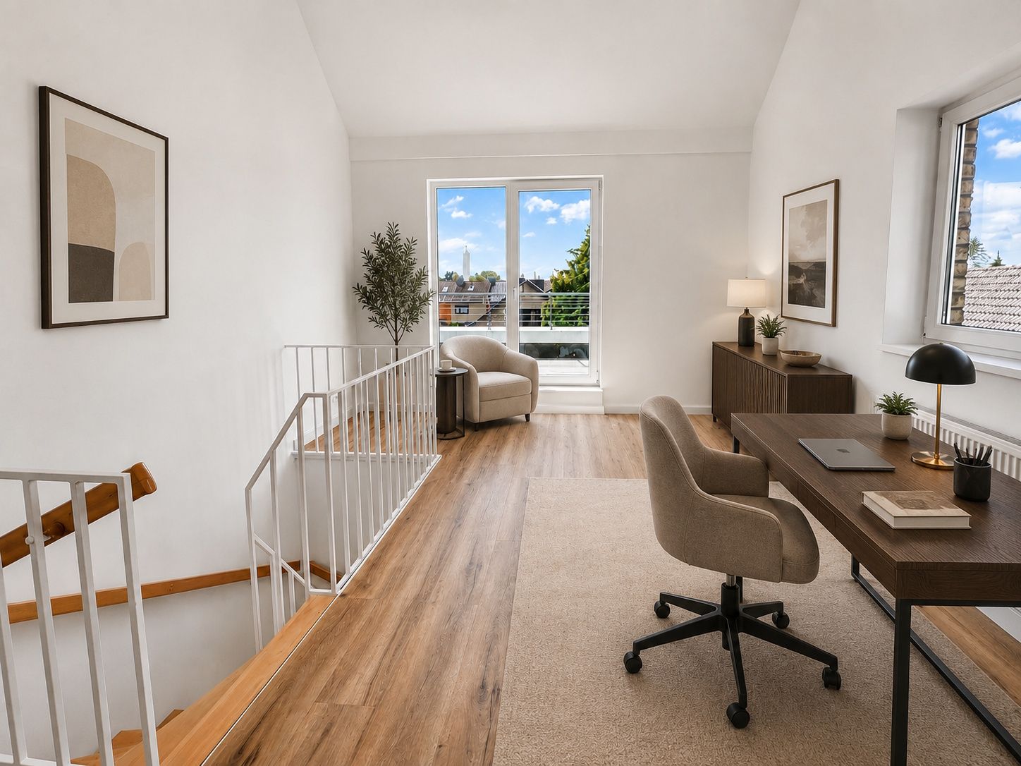 Helles Arbeitszimmer mit Schreibtisch, Stuhl, Sessel, Bildern und Zugang zu einem Balkon.